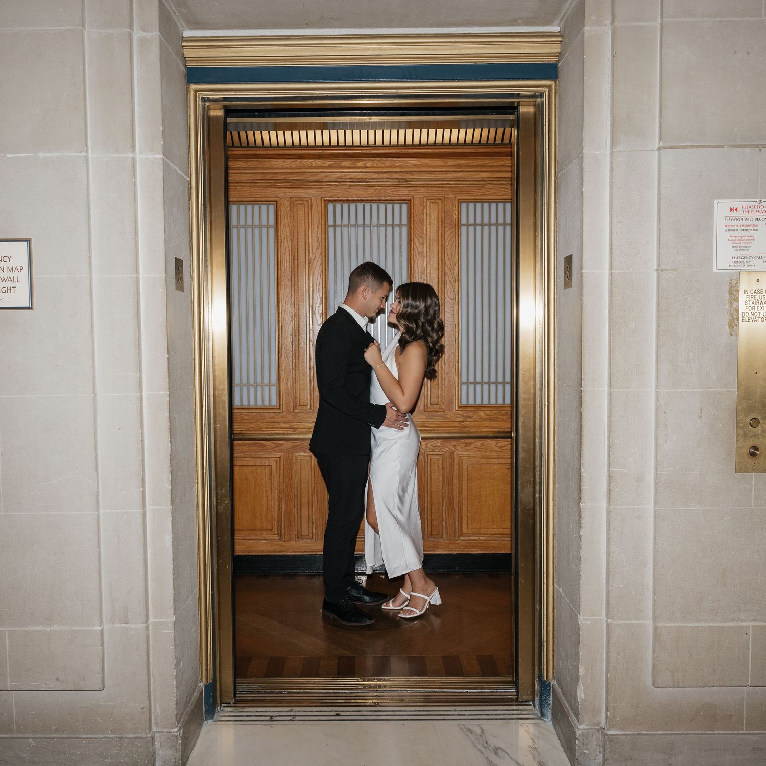 Couple sharing a moment near wooden doors in a grand marble corridor.