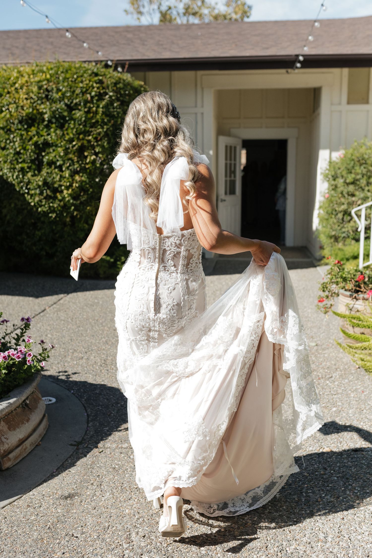 Bride in lace wedding gown walking along gravel path outside venue.
