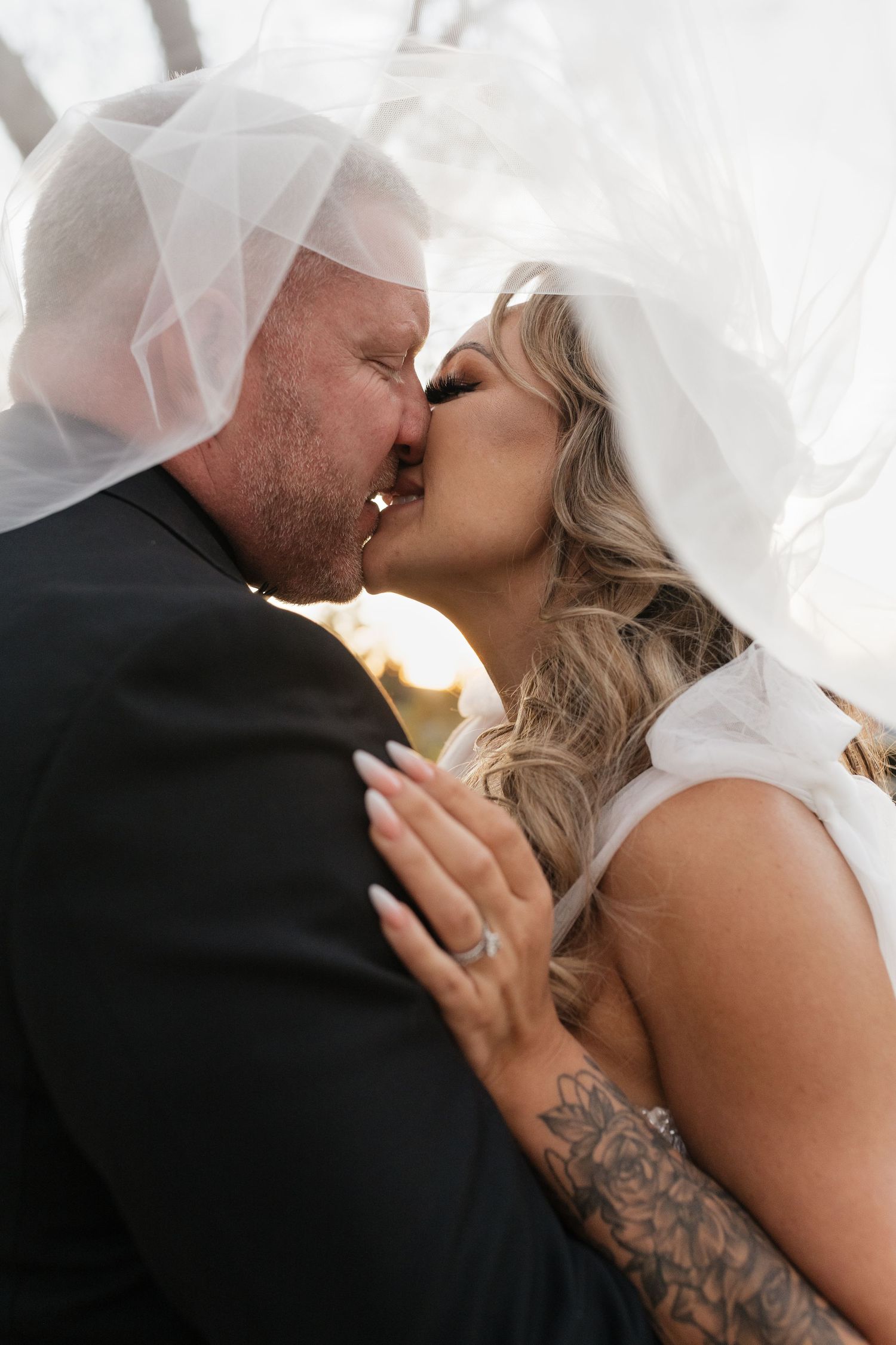 An intimate wedding portrait captured under a flowing veil during a romantic kiss.