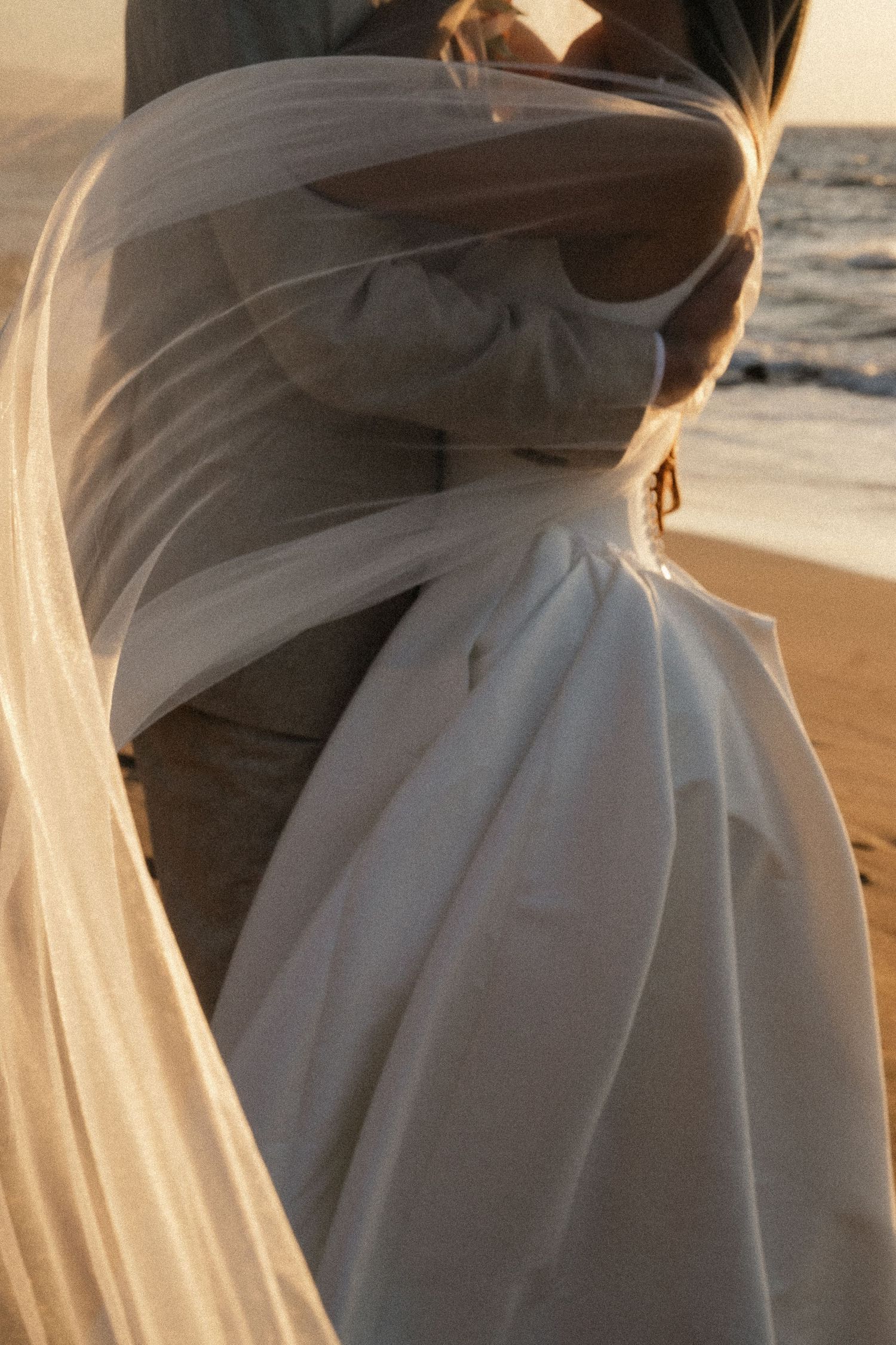 Sunlight illuminates the delicate details of a white wedding dress and veil during golden hour.