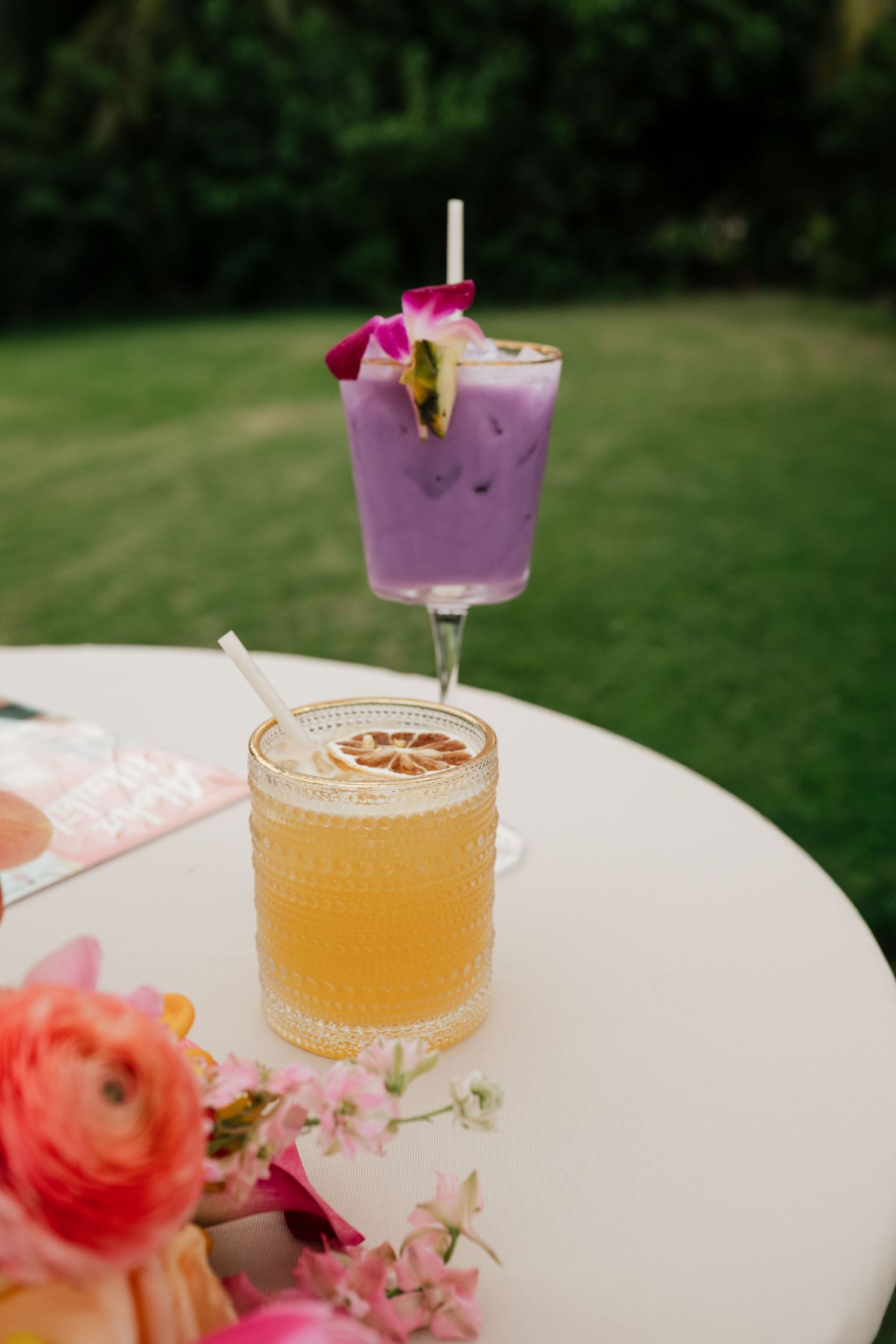 Two tropical wedding cocktails on white table, purple lavender drink and golden citrus mocktail.