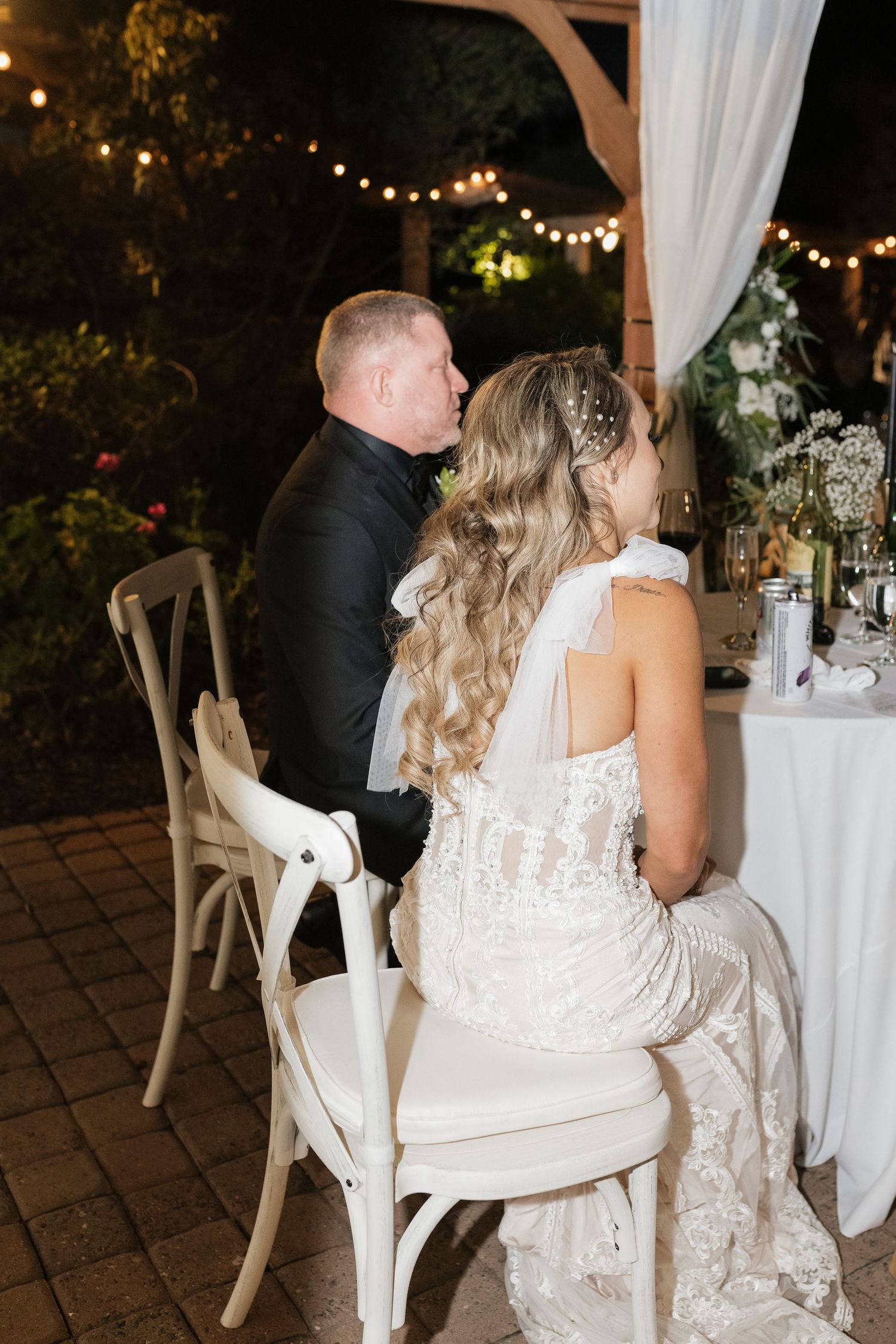 Evening reception scene with string lights and elegant table settings under draped white fabric.
