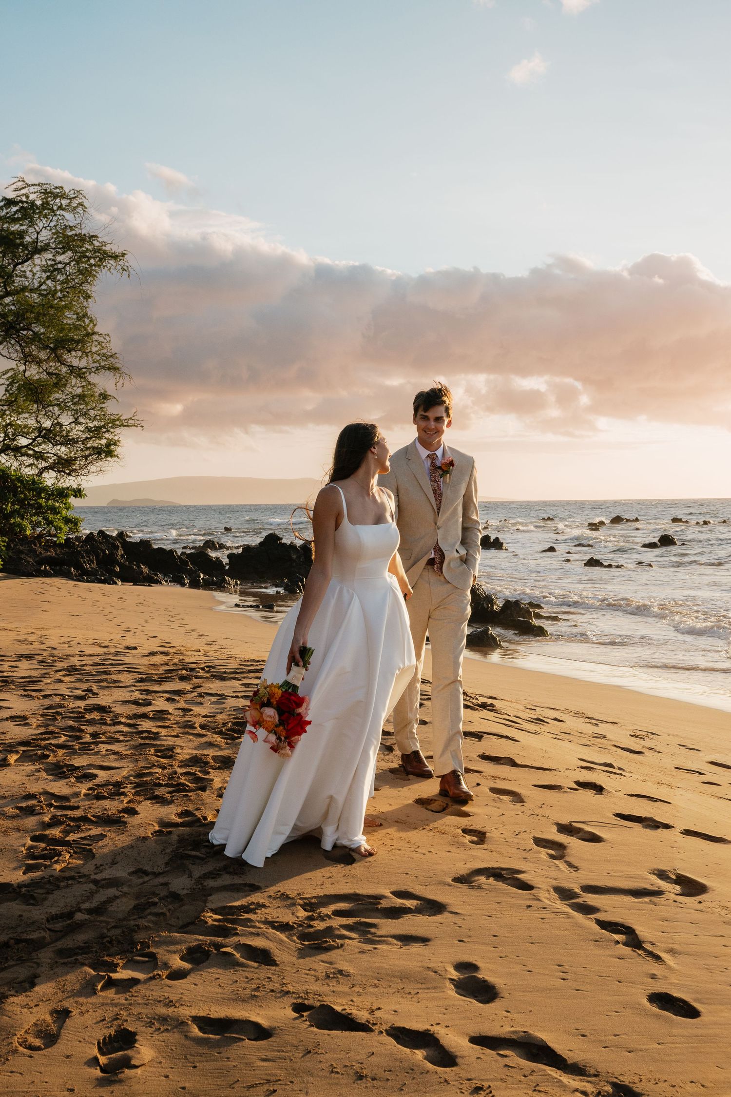 A couple shares a romantic moment on a sandy beach at sunset with waves crashing in the background.