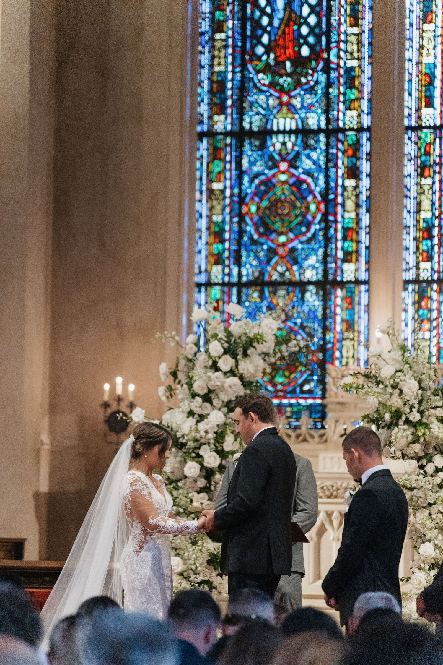 Wedding ceremony in progress with stained glass windows and white floral arrangements.