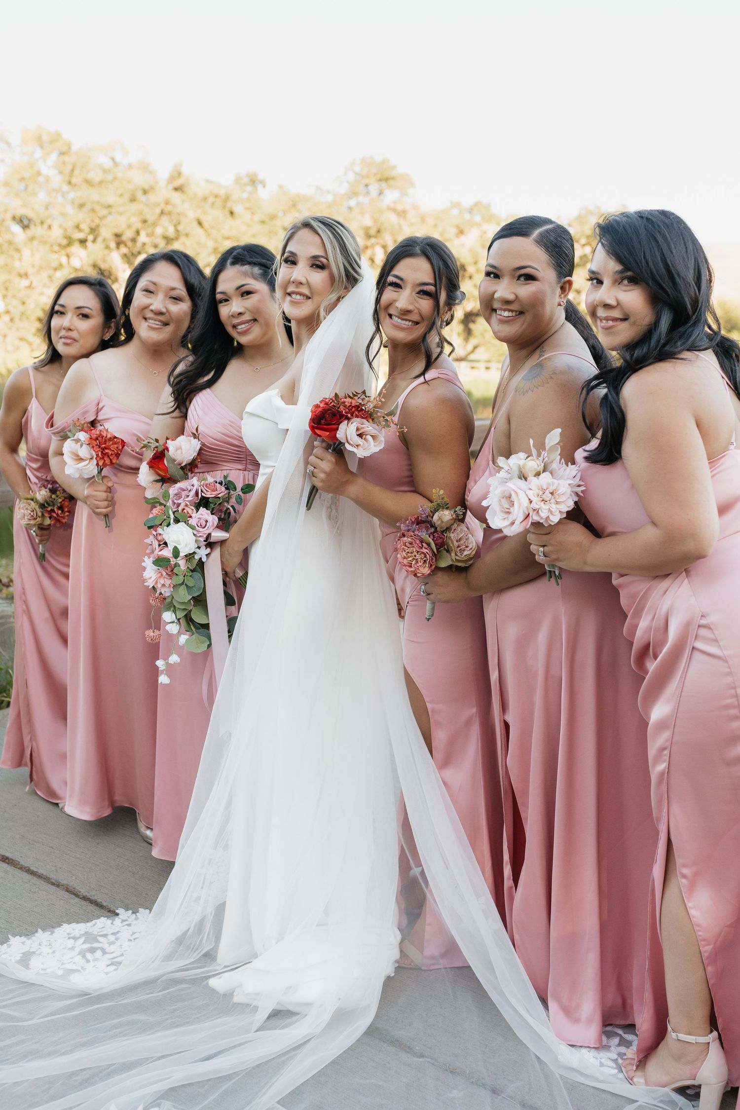 Bridal party in pink dresses poses together holding floral bouquets.