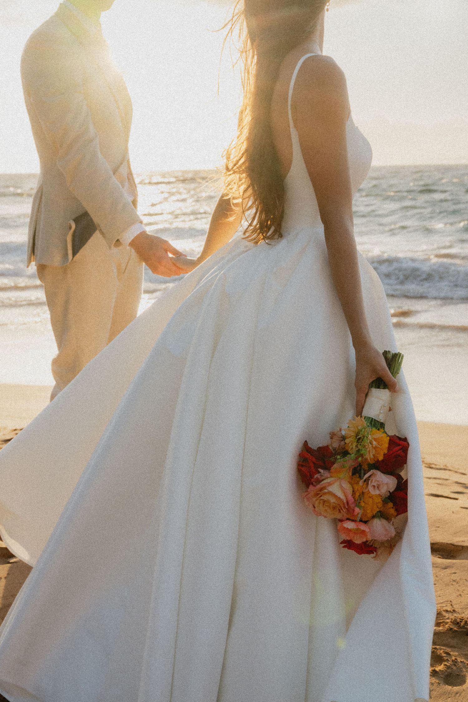 White wedding dress flowing in the ocean breeze at sunset on a tropical beach.