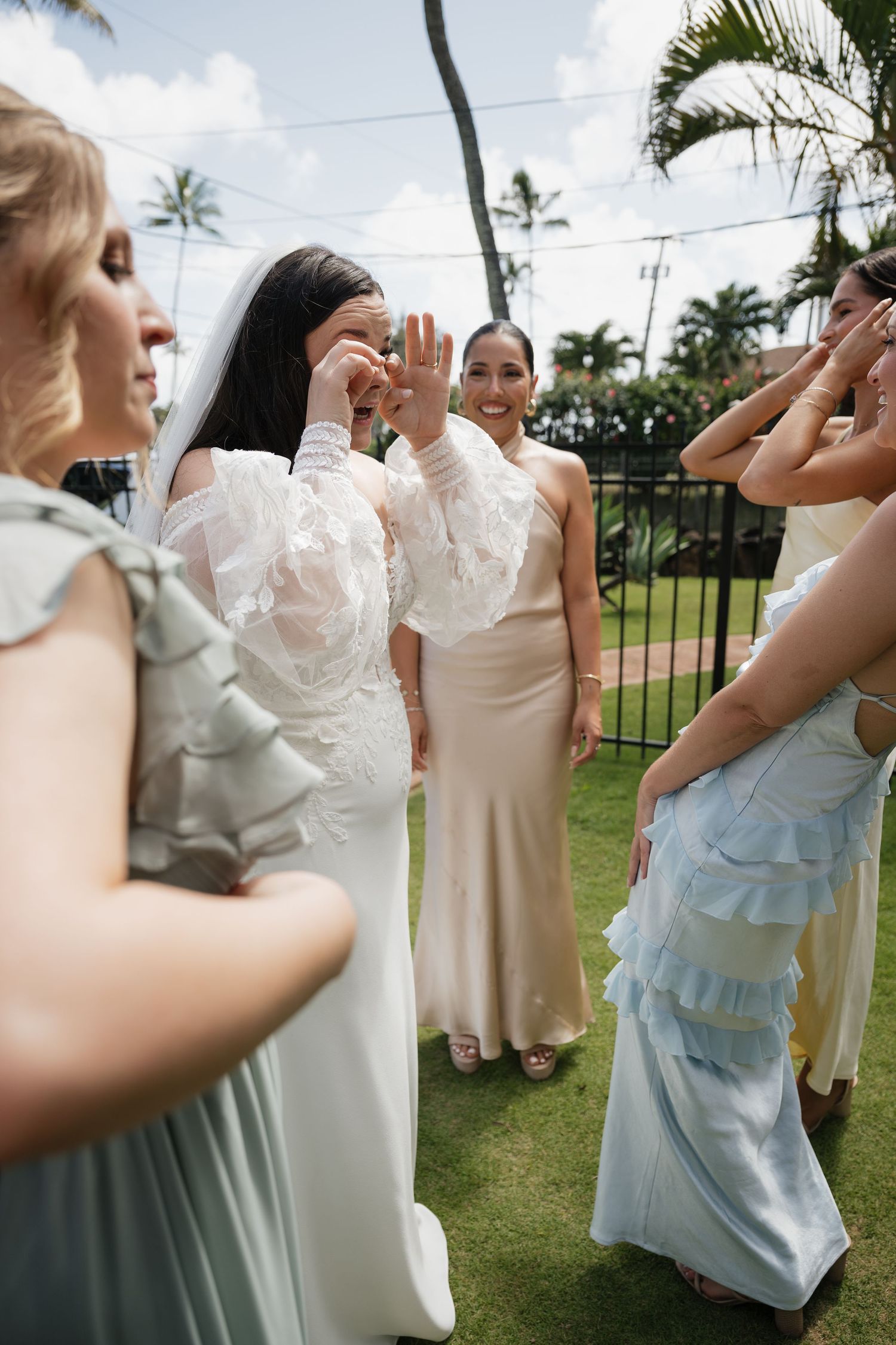 Wedding party celebrates outdoors with expressive gestures on tropical garden lawn.