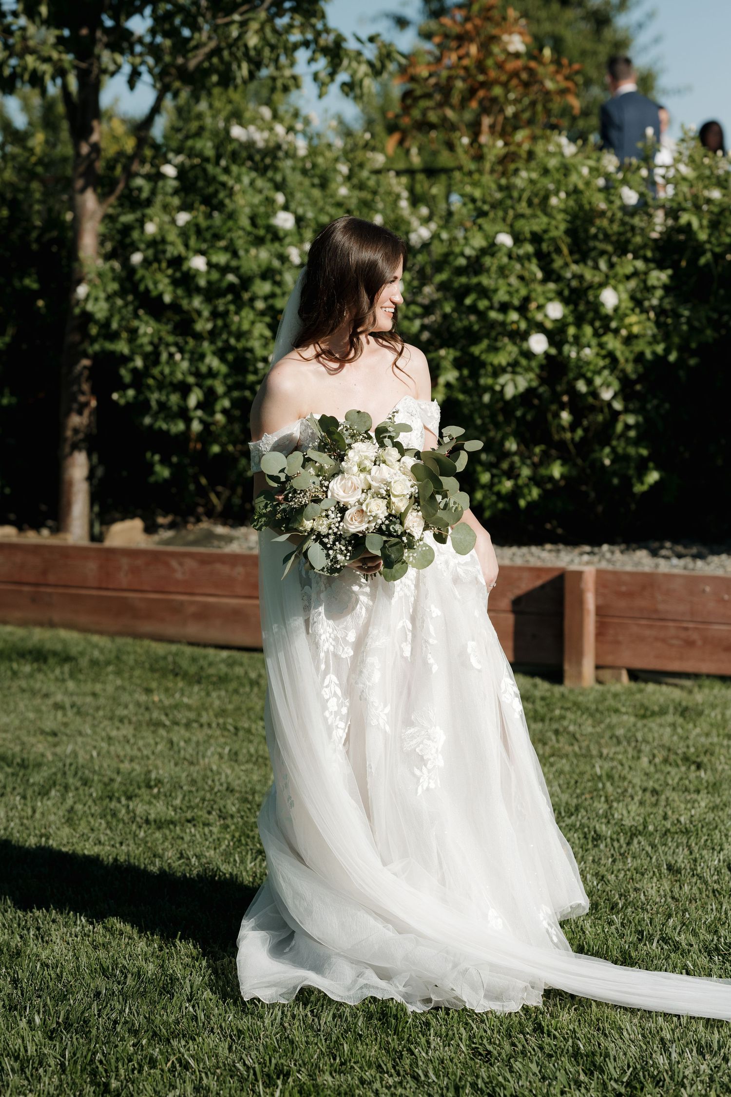 White wedding dress flows gracefully across green lawn during outdoor bridal portraits.