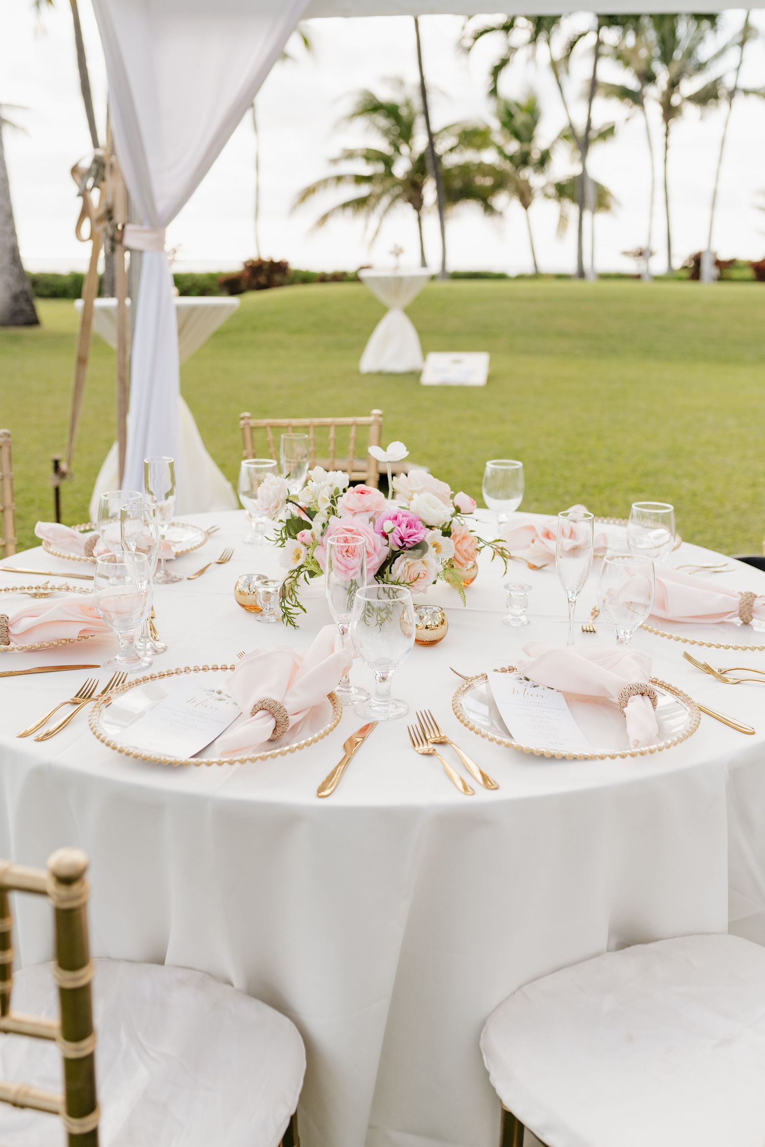 Elegant wedding reception table settings with white linens and pink floral centerpieces under a tent.