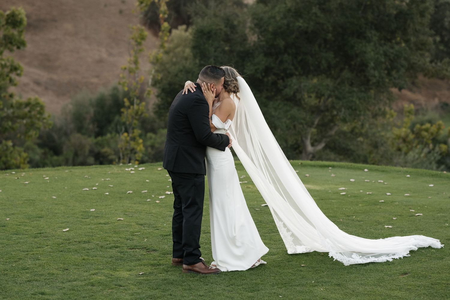 Wedding couple sharing intimate moments on a hillside with flowing white veil and dress.