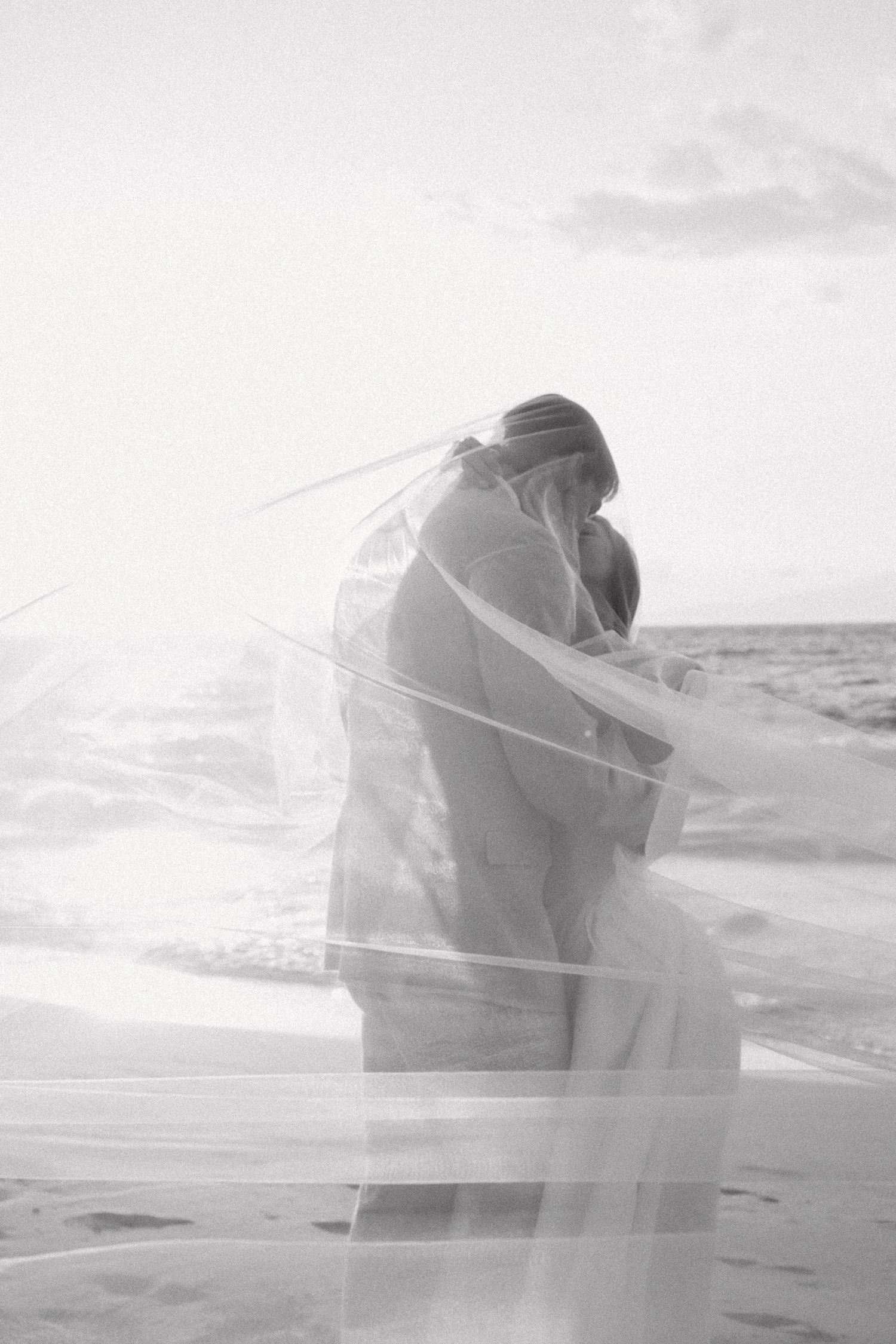 Ethereal beach wedding photos with flowing veil against ocean backdrop.