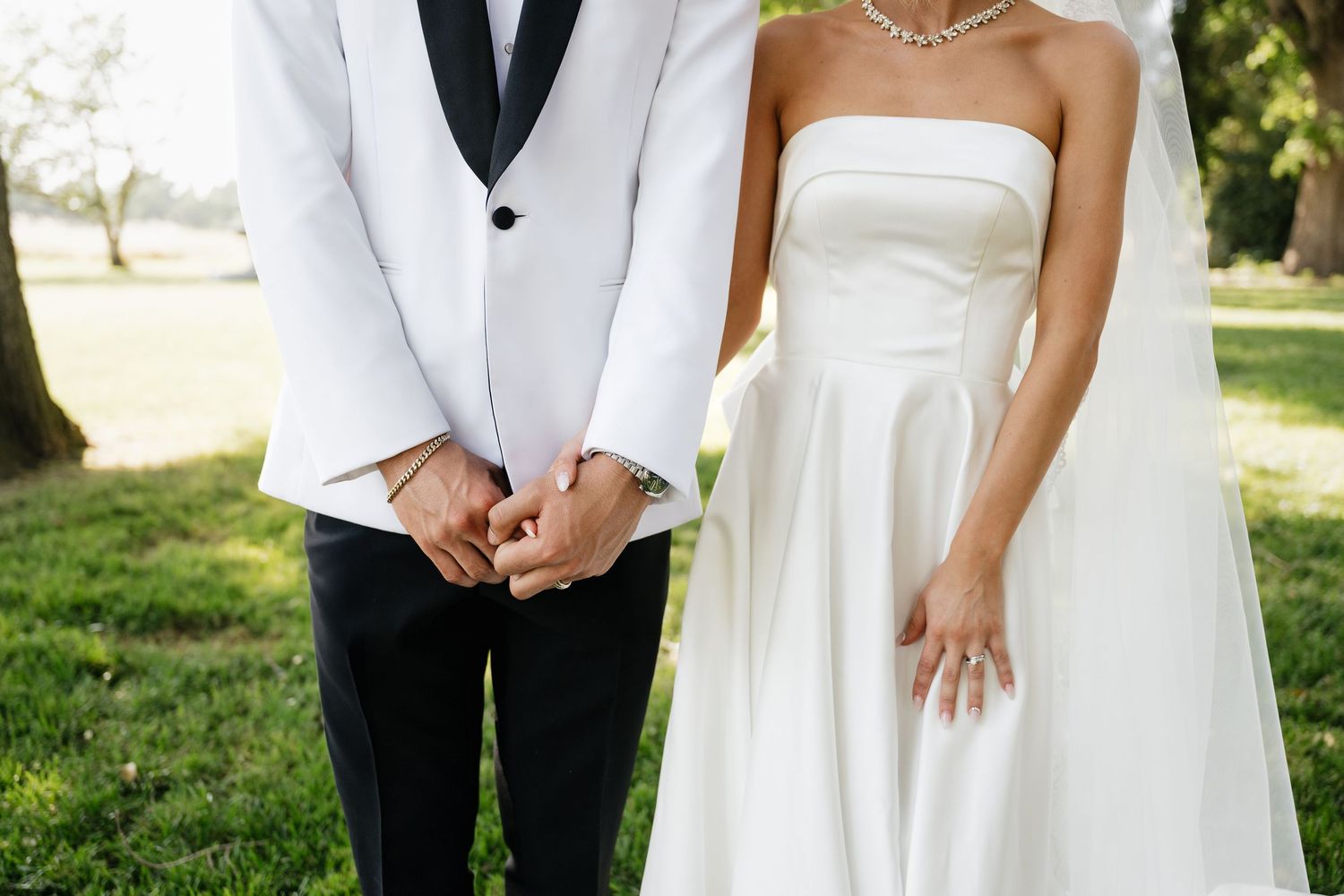 Elegant wedding party in white dresses and formal attire pose outdoors.