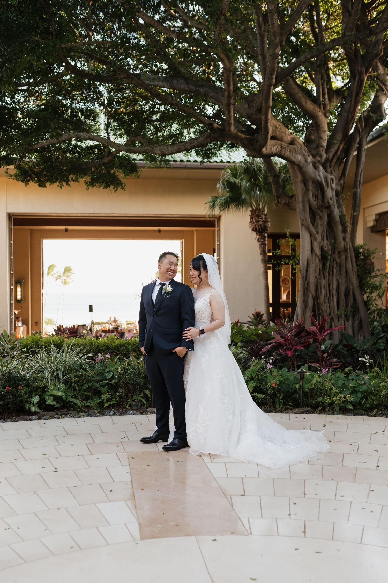 Wedding couple walking under banyan trees at a tropical resort venue.