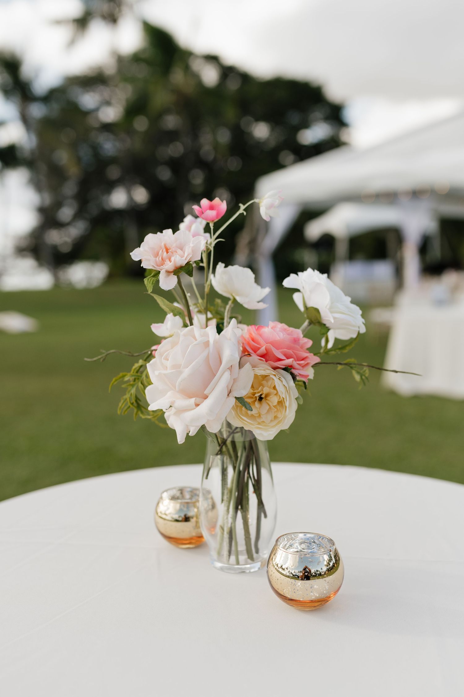 Delicate pink and white roses in gold-rimmed vases as wedding table centerpieces.