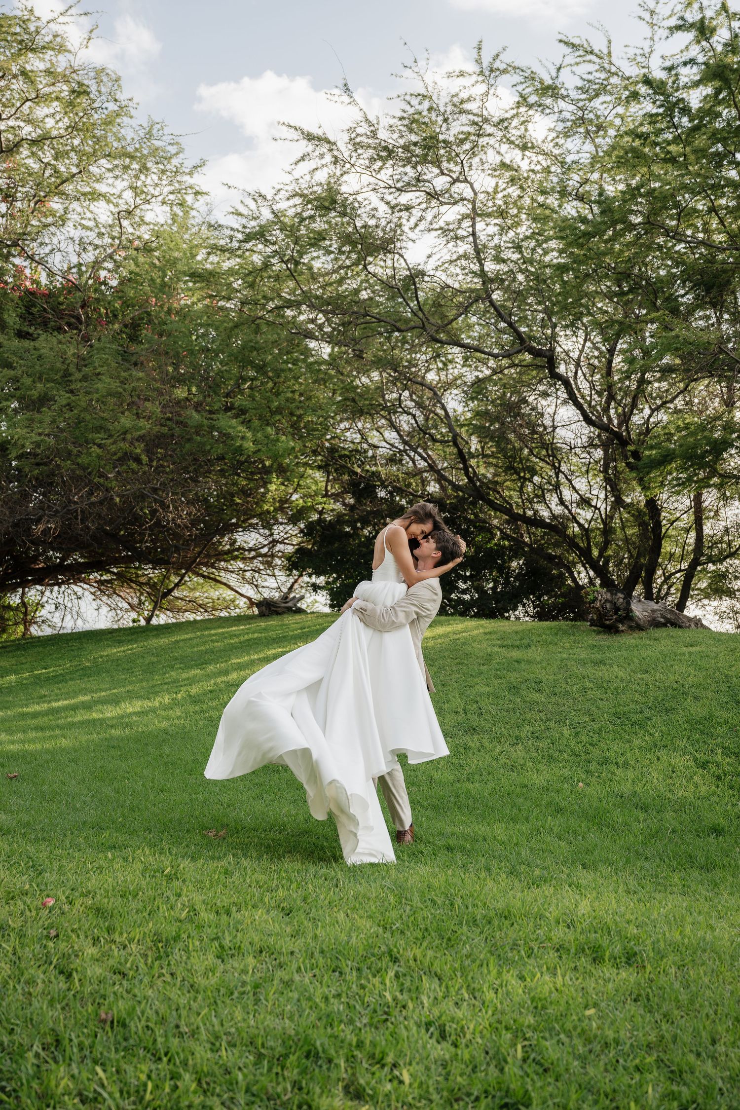 A flowing white wedding dress twirls gracefully across a lush green hillside on a sunny day.