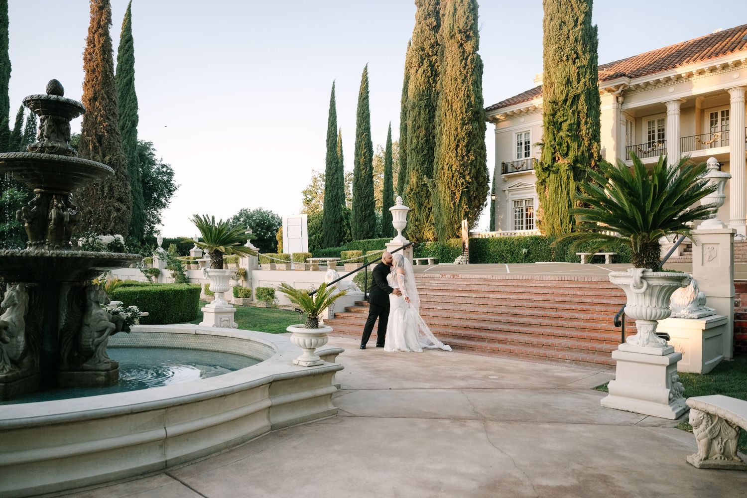 Panoramic view of a Mediterranean-style courtyard with cypress trees and classical architecture details.