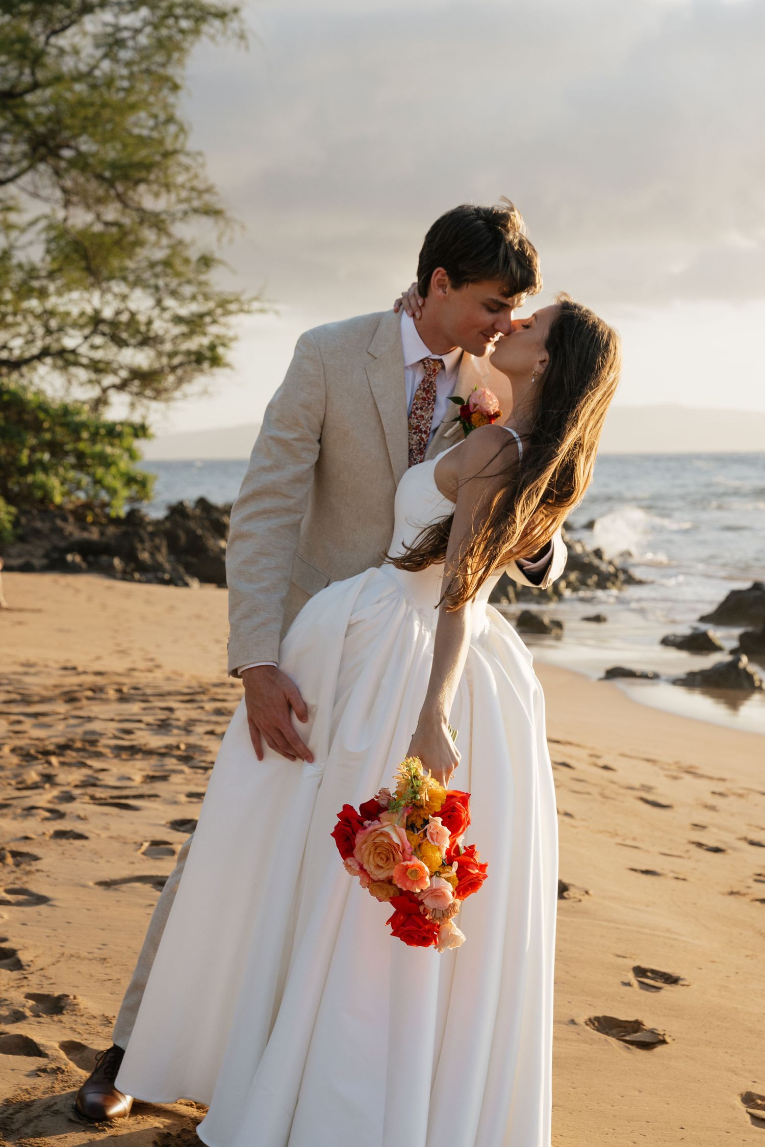 A romantic beach wedding scene at sunset with vibrant floral bouquet and sandy shoreline.