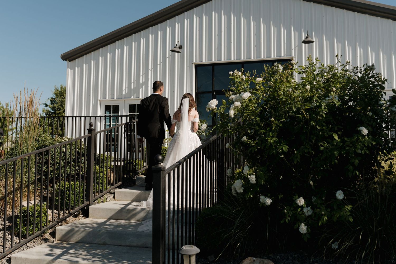 Modern white barn exterior decorated with string lights and floral arrangements for a wedding celebration.