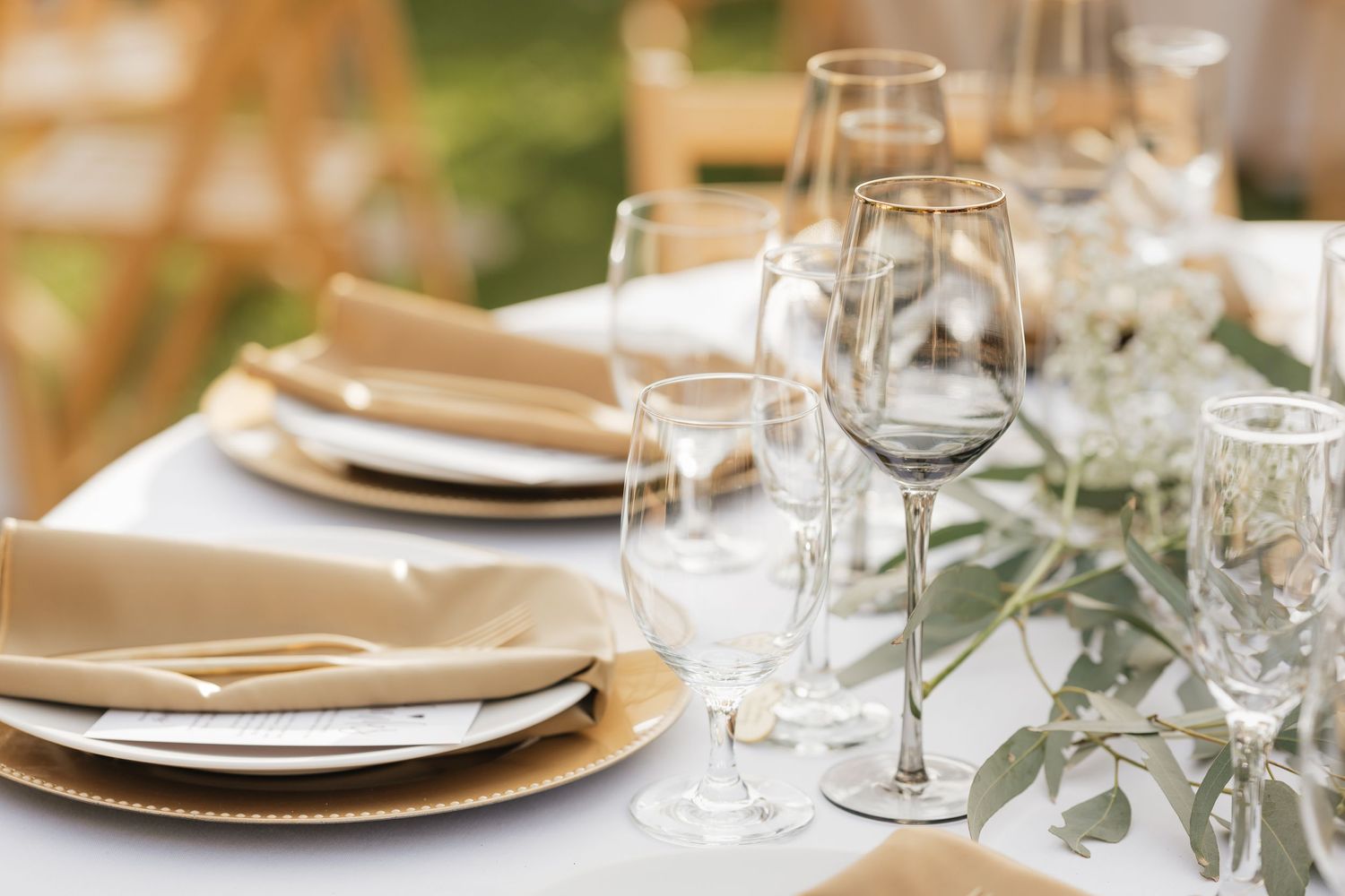 Close-up of wedding reception table settings with gold charger plates and white linens.