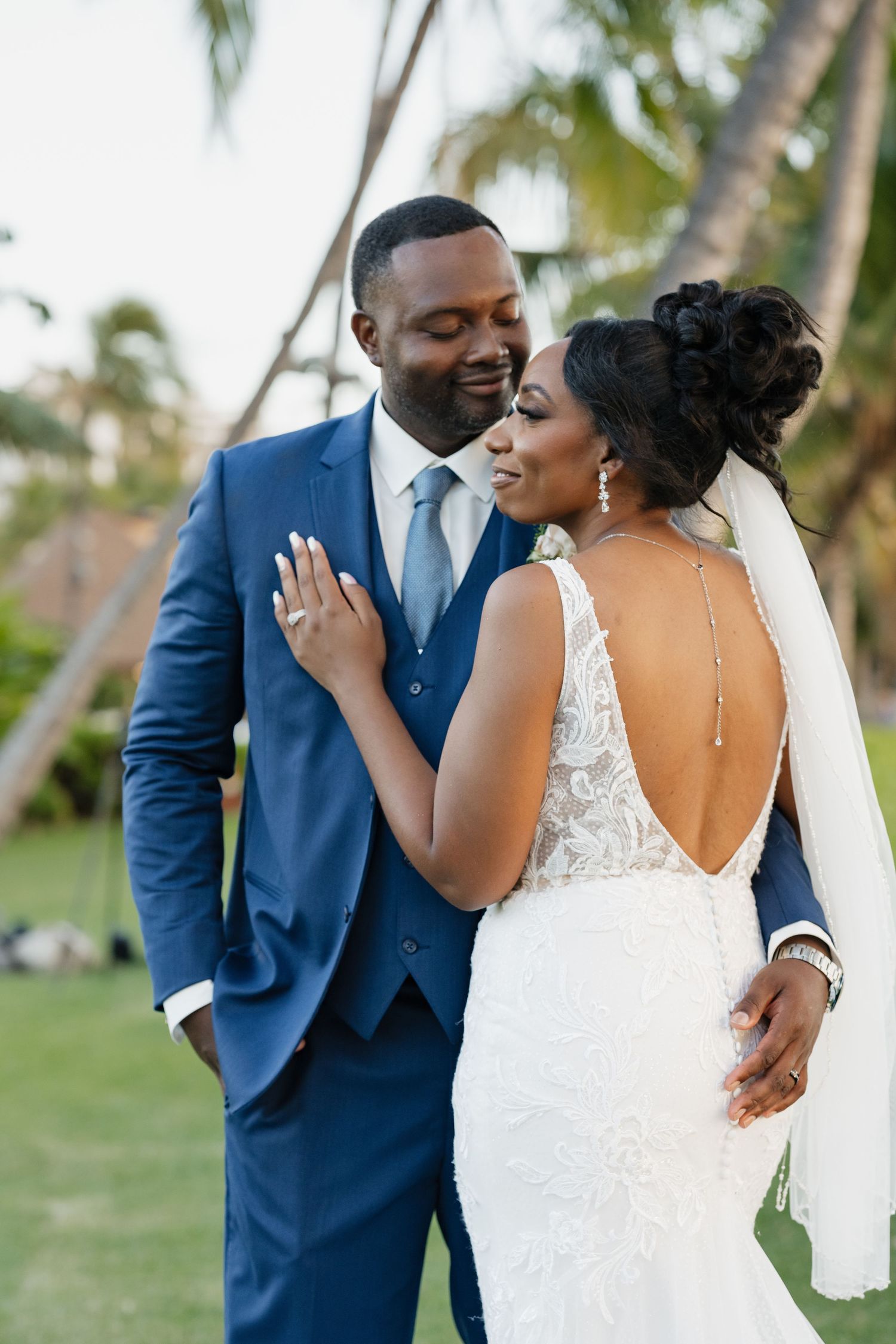 Couple shares intimate moment during outdoor wedding portraits with palm trees in background.