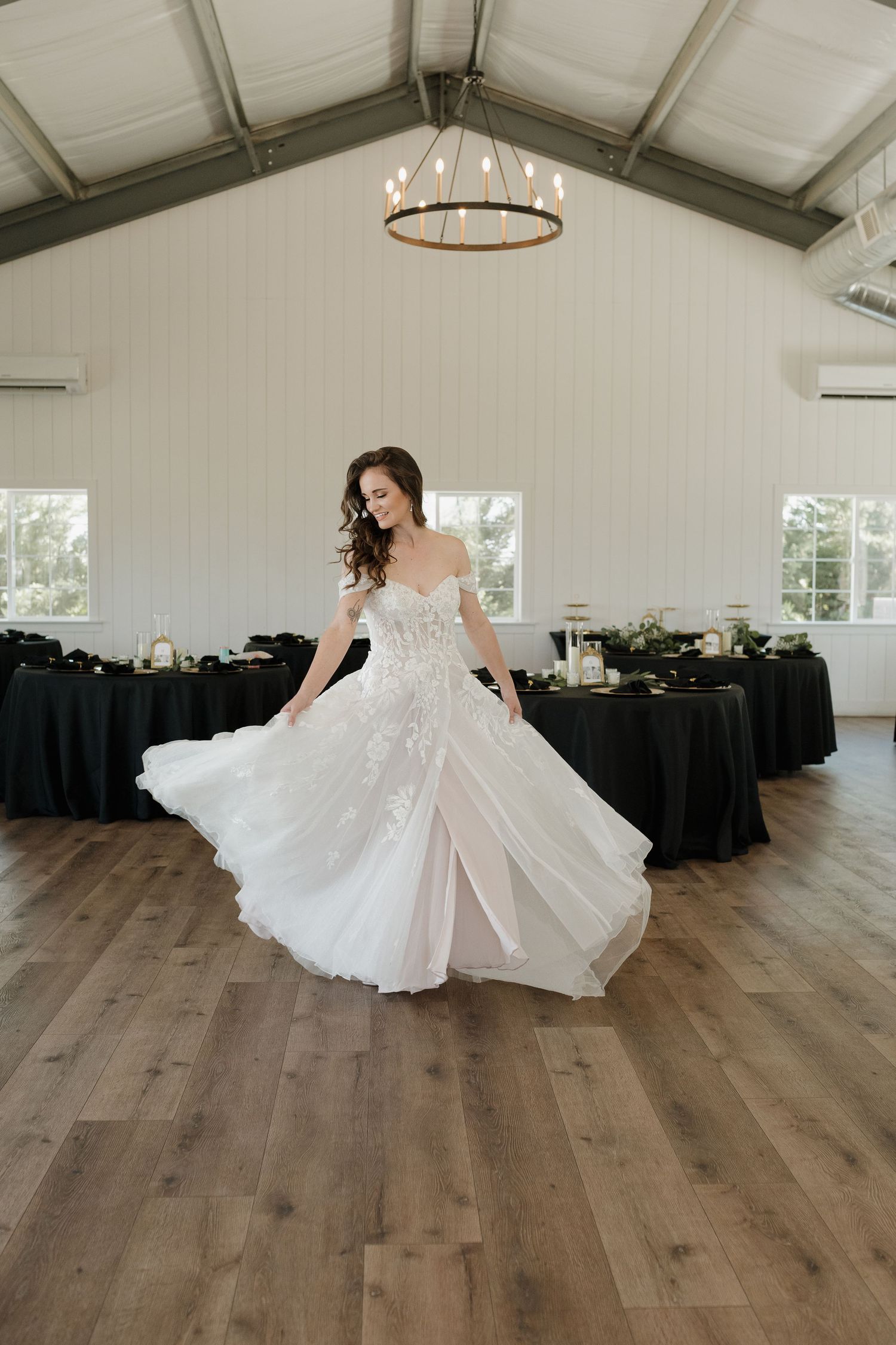 White wedding dress twirls on wooden floor in elegant reception venue with chandeliers.