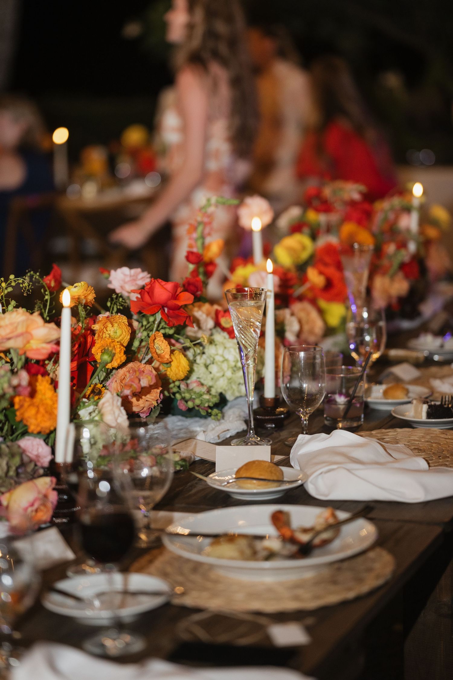 Elegant wedding reception table setting with colorful floral centerpieces and candlelight.