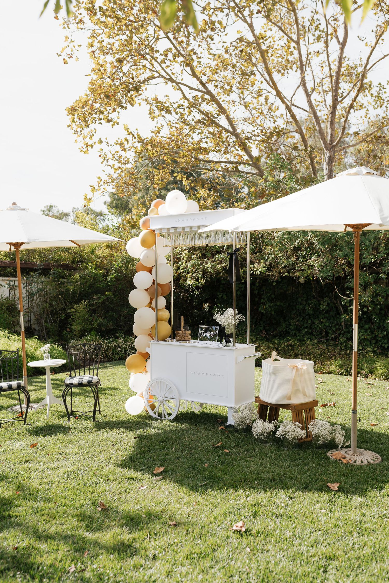 Elegant outdoor wedding setup with white umbrellas, chairs, and balloon decorations in a garden setting.
