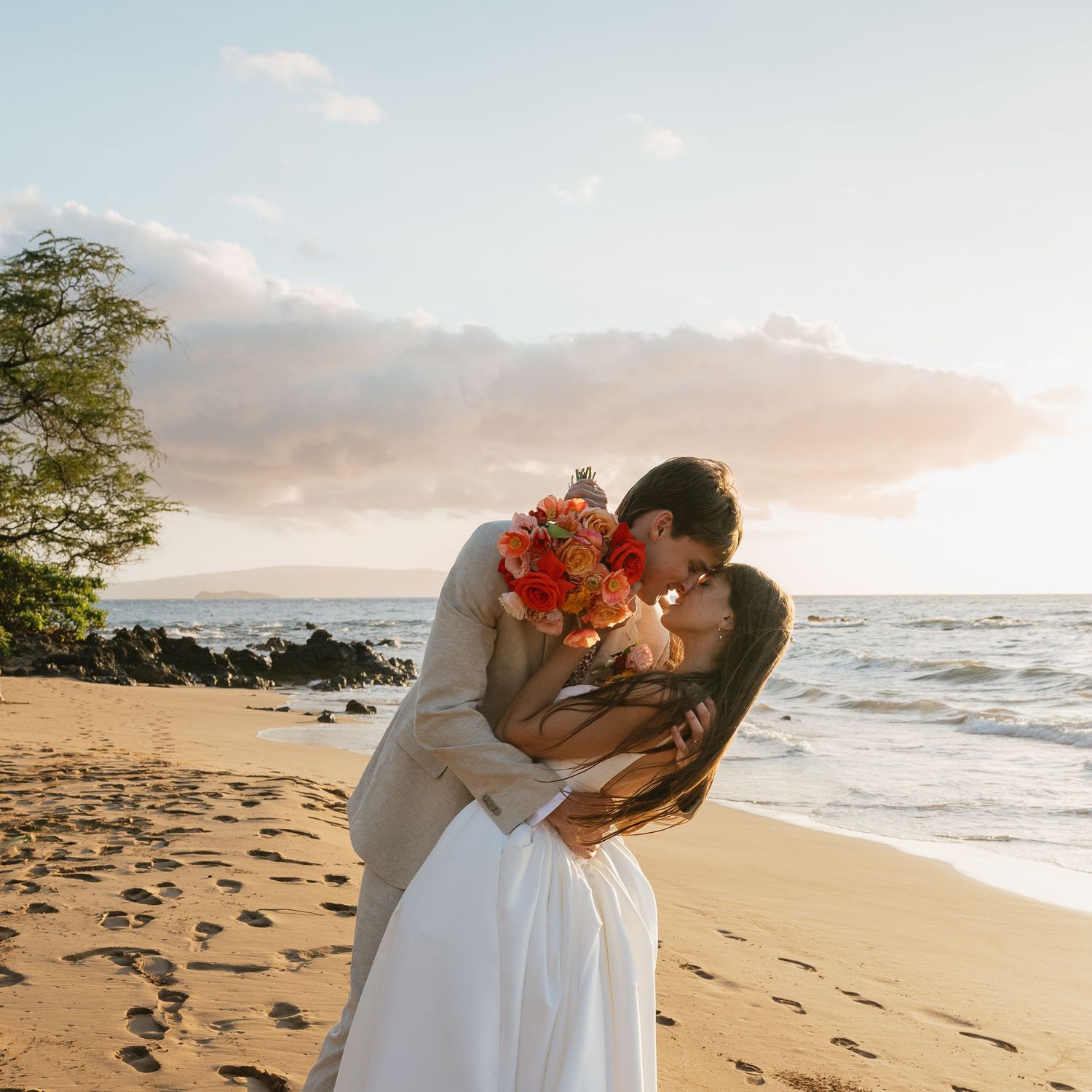 Romantic sunset beach wedding moment with tropical flowers and golden light on sandy shore.