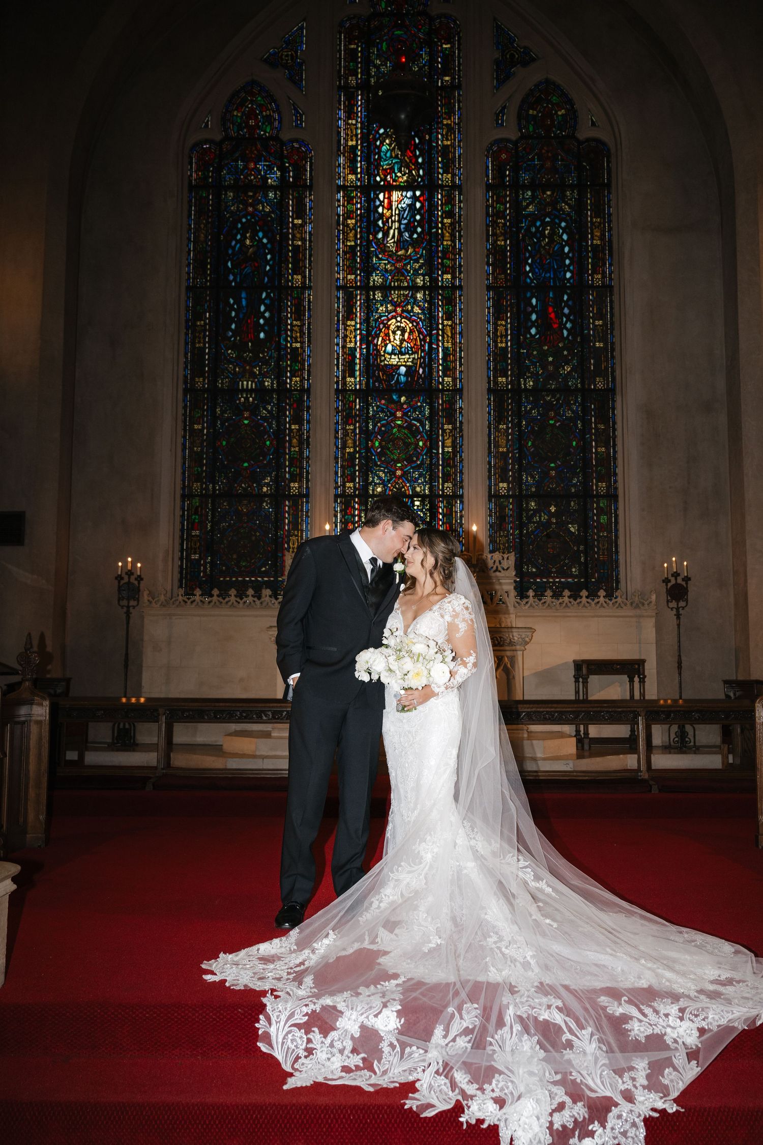 Dramatic church wedding portrait with ornate stained glass windows and flowing lace train.