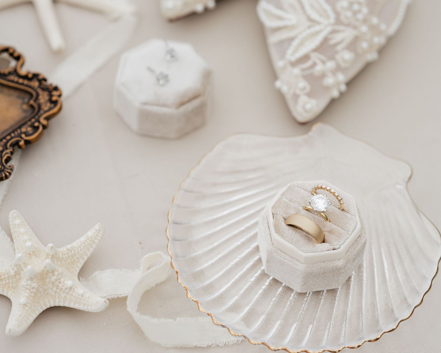 Elegant wedding rings displayed in a white velvet box on a seashell dish, surrounded by starfish and vintage decor.