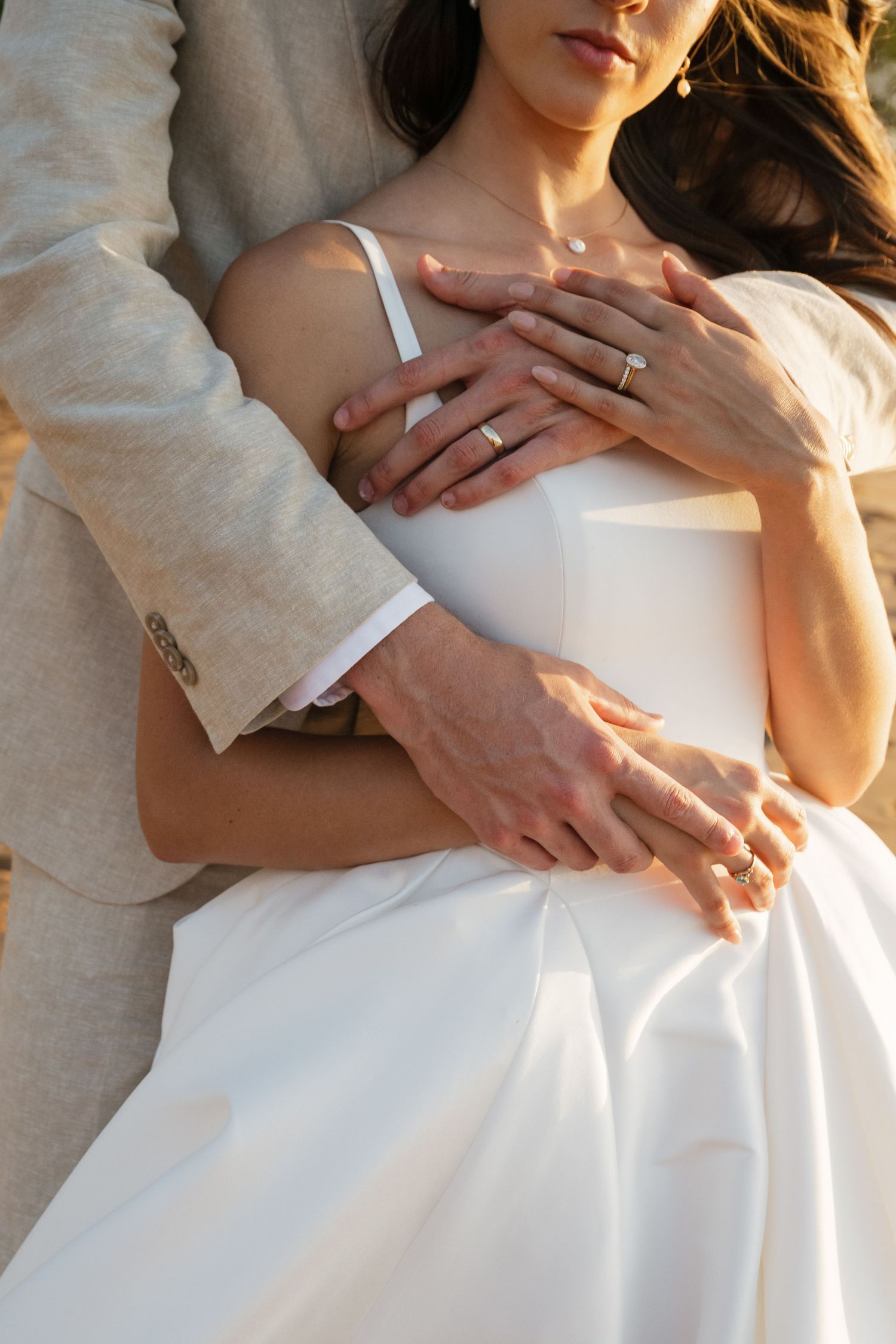 Close-up of hands wearing wedding rings embracing in white wedding attire.