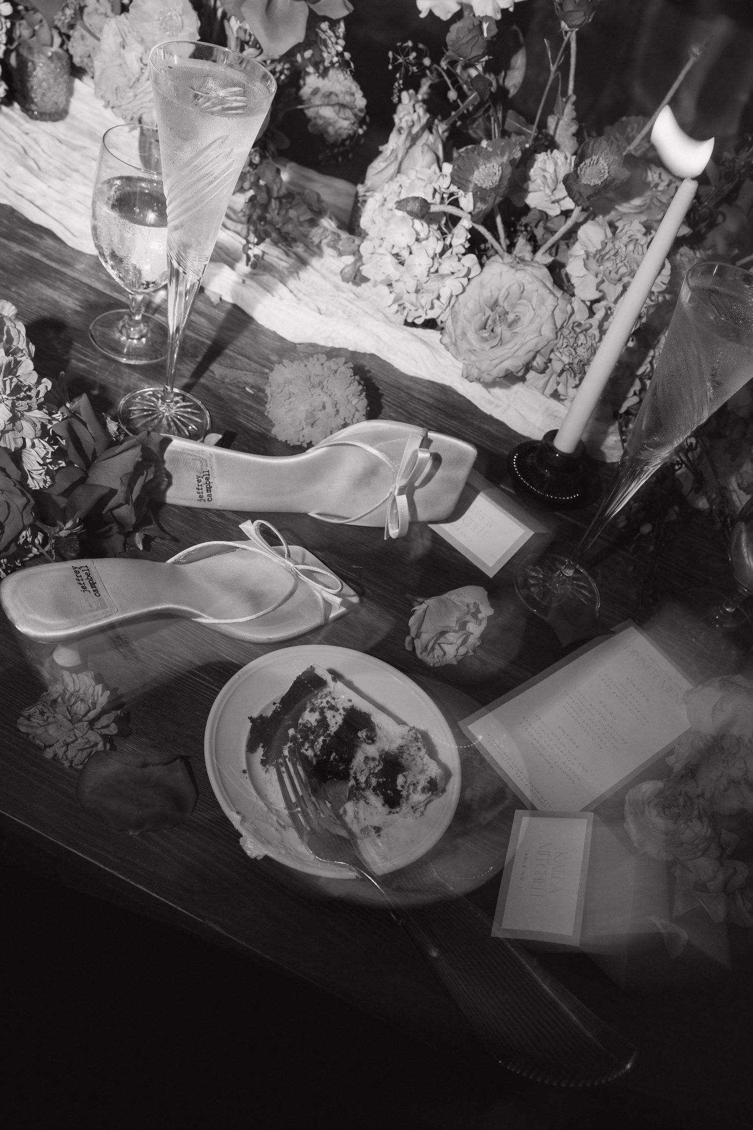 Black and white image of elegant place settings with floral arrangements at a formal dining table.