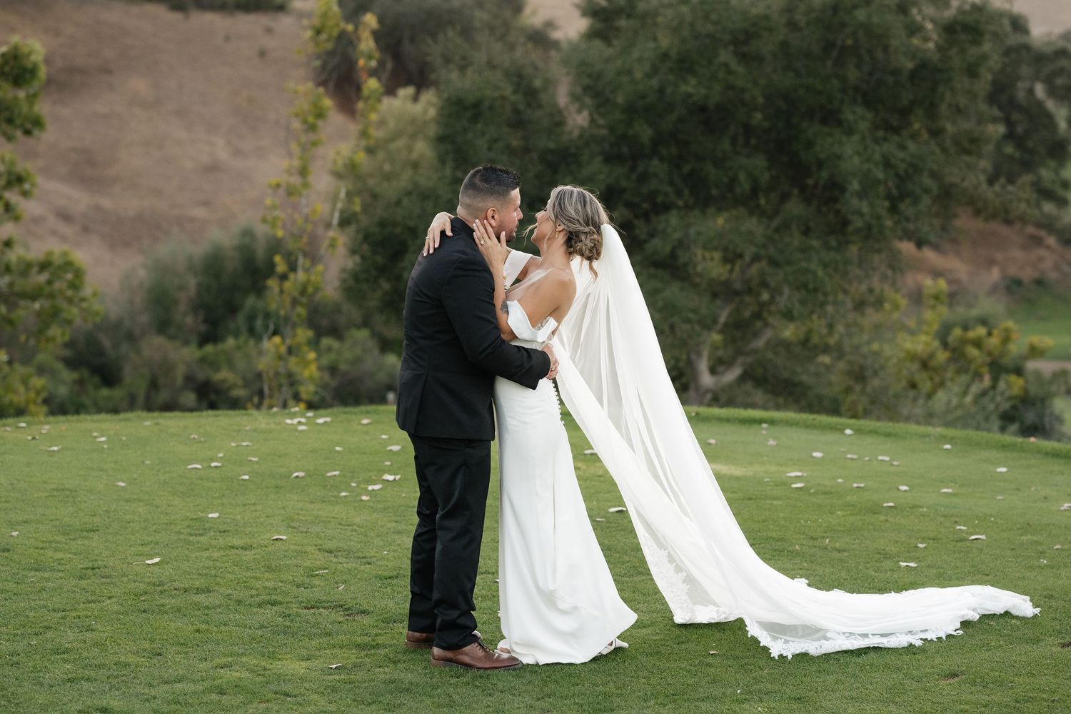 Wedding party poses for photos on grassy hillside during golden hour.