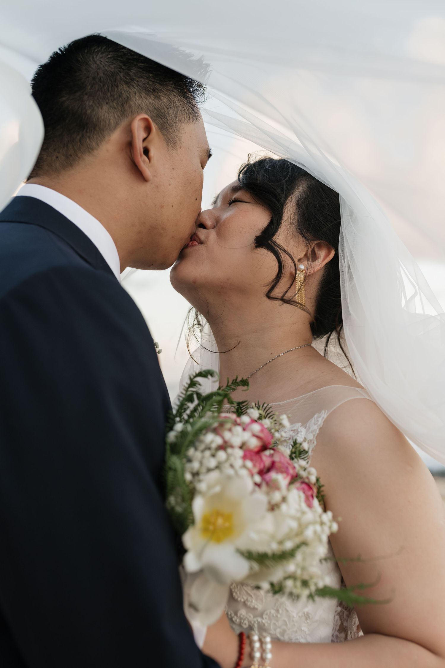 A romantic wedding couple sharing an intimate kiss while the bride holds a delicate bouquet.