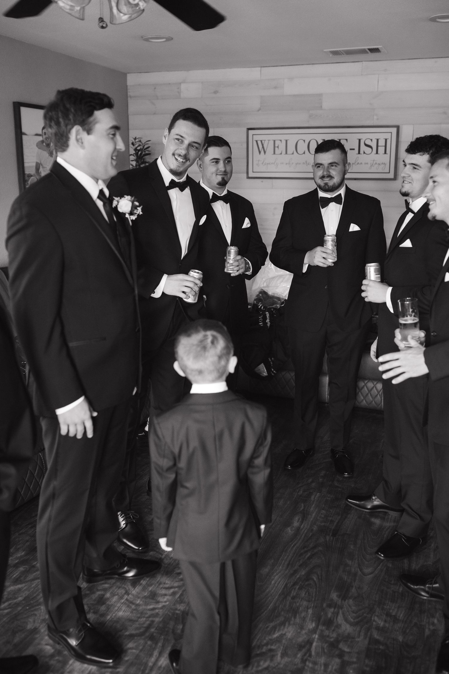 Groomsmen in formal black tuxedos gather for candid moments before the ceremony.