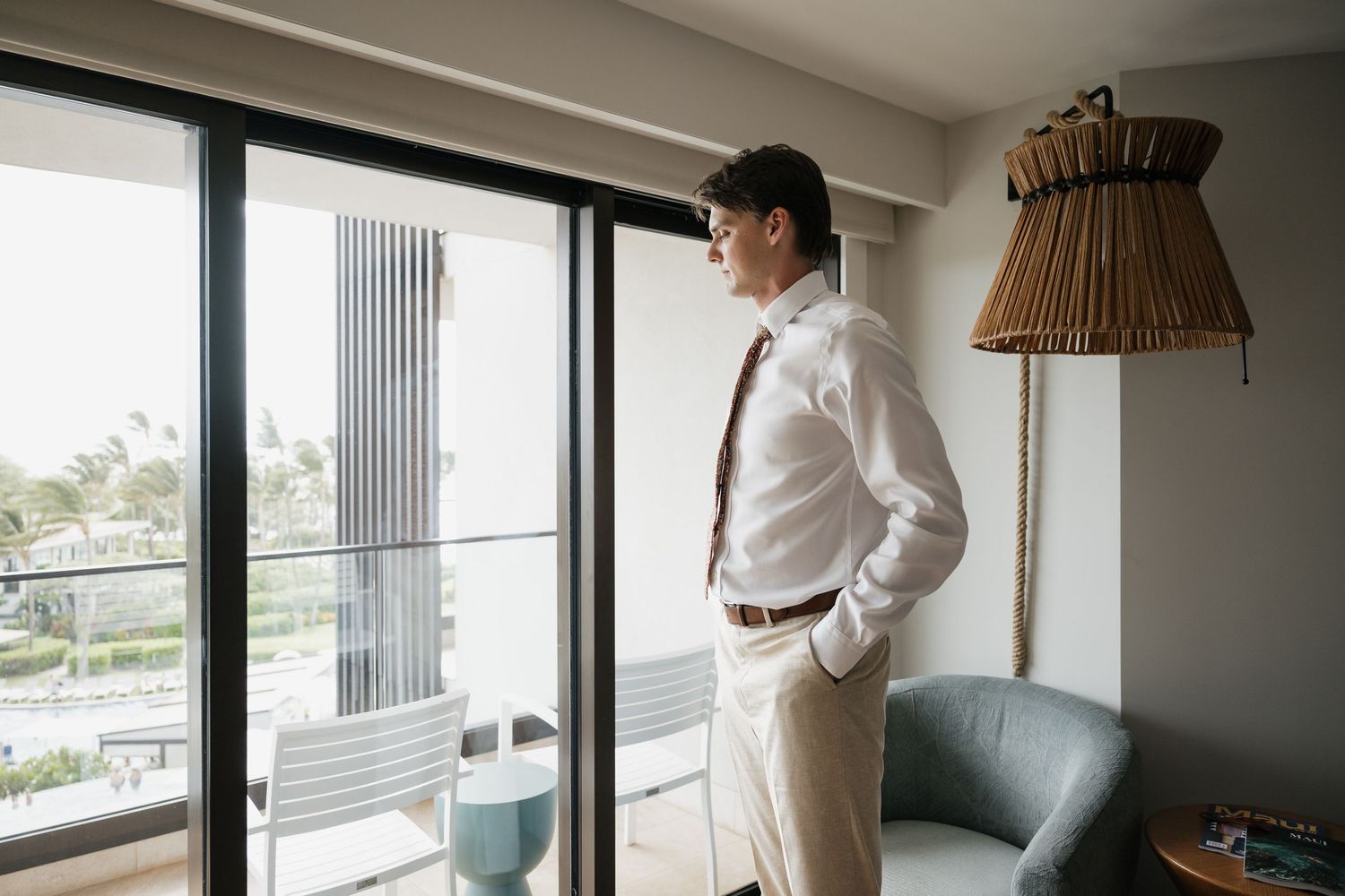 Person in white shirt standing by window in modern minimalist interior with light gray walls and natural lighting.