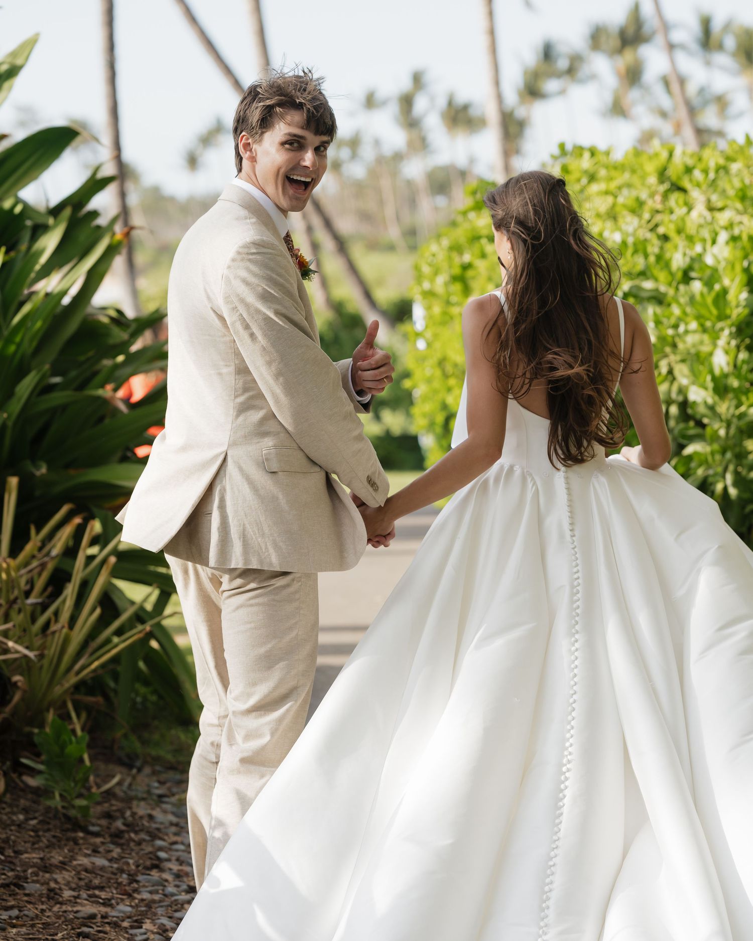 Couple in wedding attire walking through a garden setting with flowing white dress.