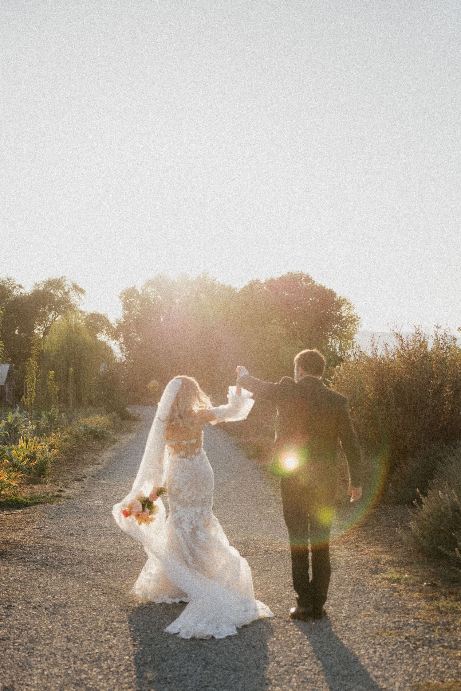 Romantic sunset wedding photos on a gravel path with dramatic backlighting.