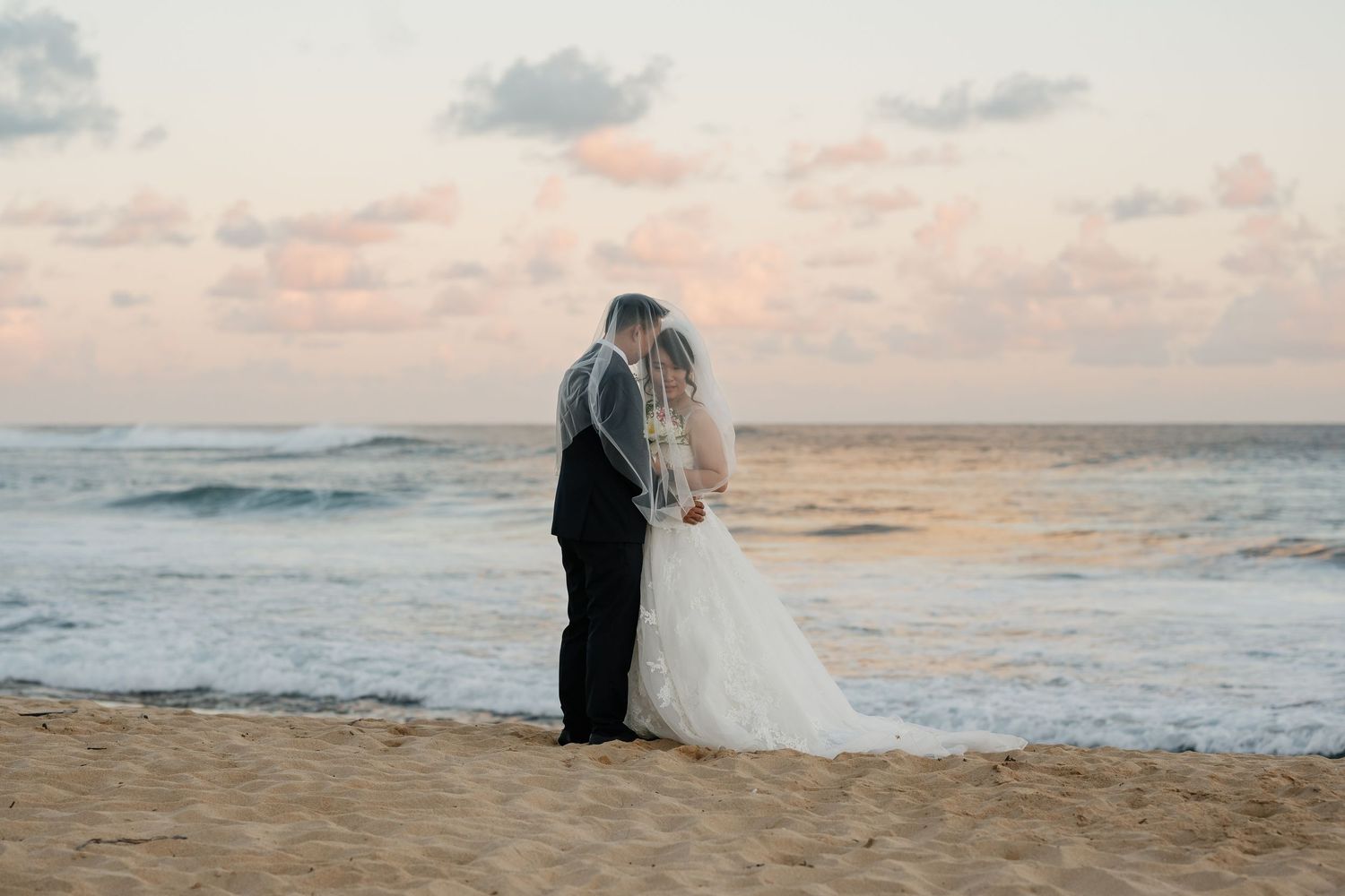 A couple shares a romantic moment on a beach at sunset with waves crashing in the background.