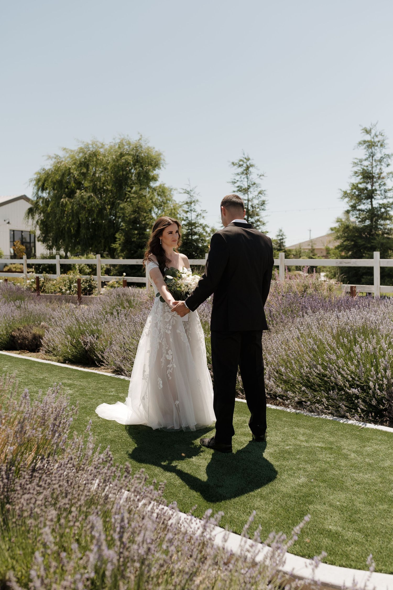 Newlyweds walking through garden path lined with blooming lavender bushes.
