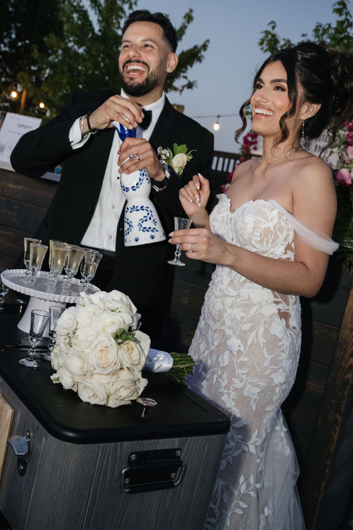 A wedding celebration at dusk with guests gathered around a black table outdoors.
