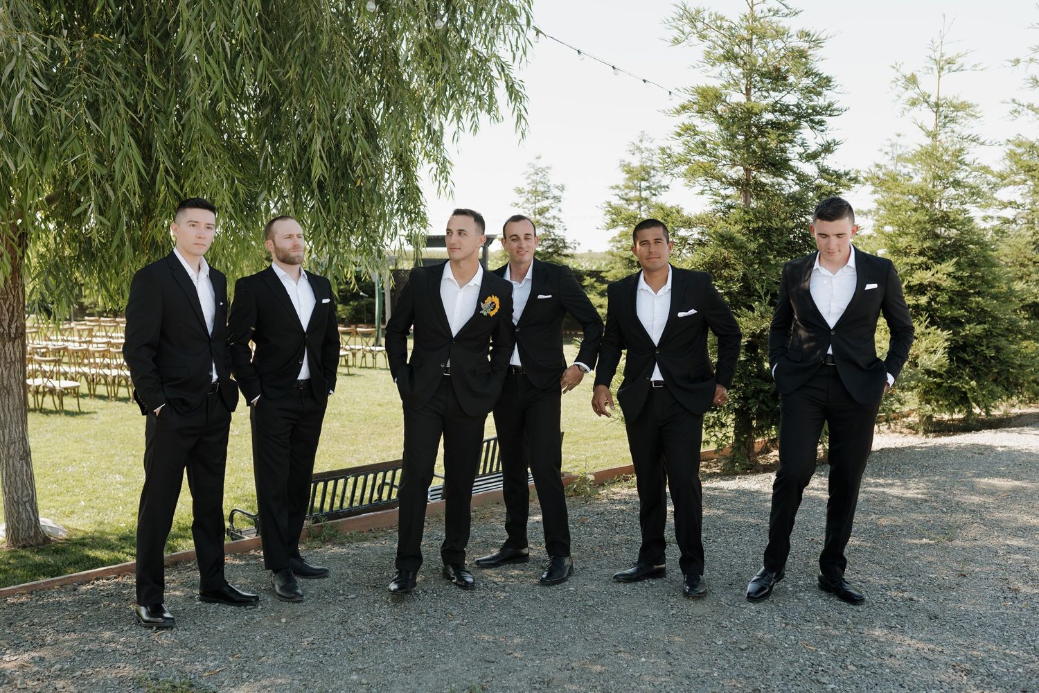 Groomsmen in formal black and white attire pose casually outdoors.