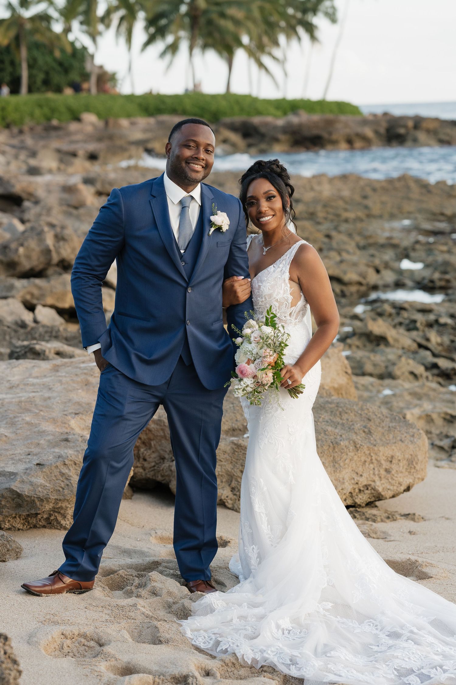 Wedding photo session on rocky beach with palm trees and ocean view.