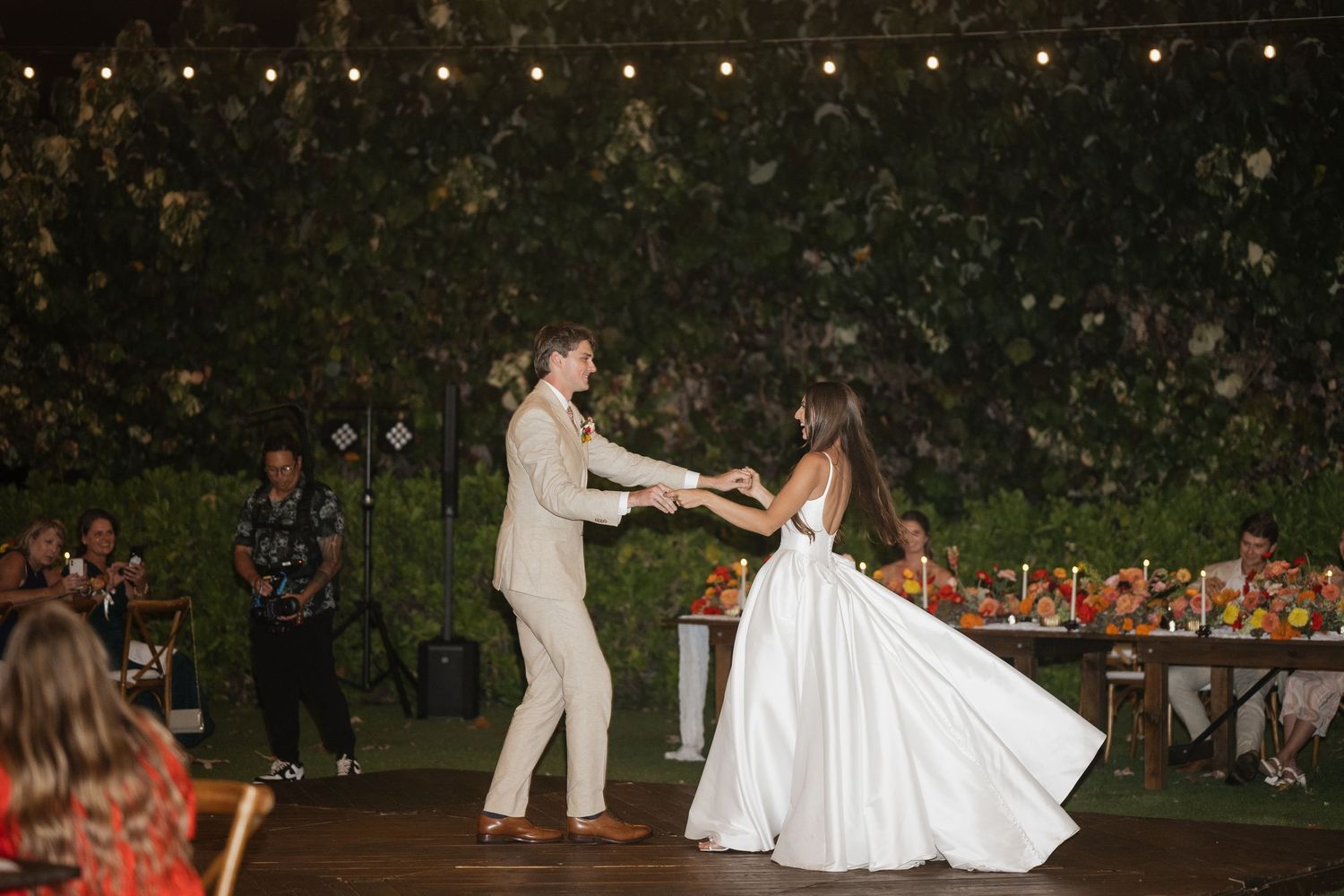 Couple dancing under string lights at an outdoor wedding reception.