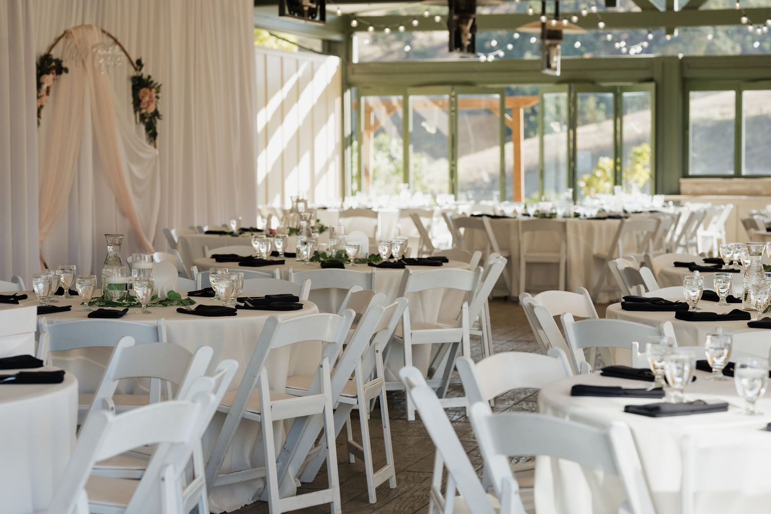 Wedding reception venue set with white chairs and tables under string lights.