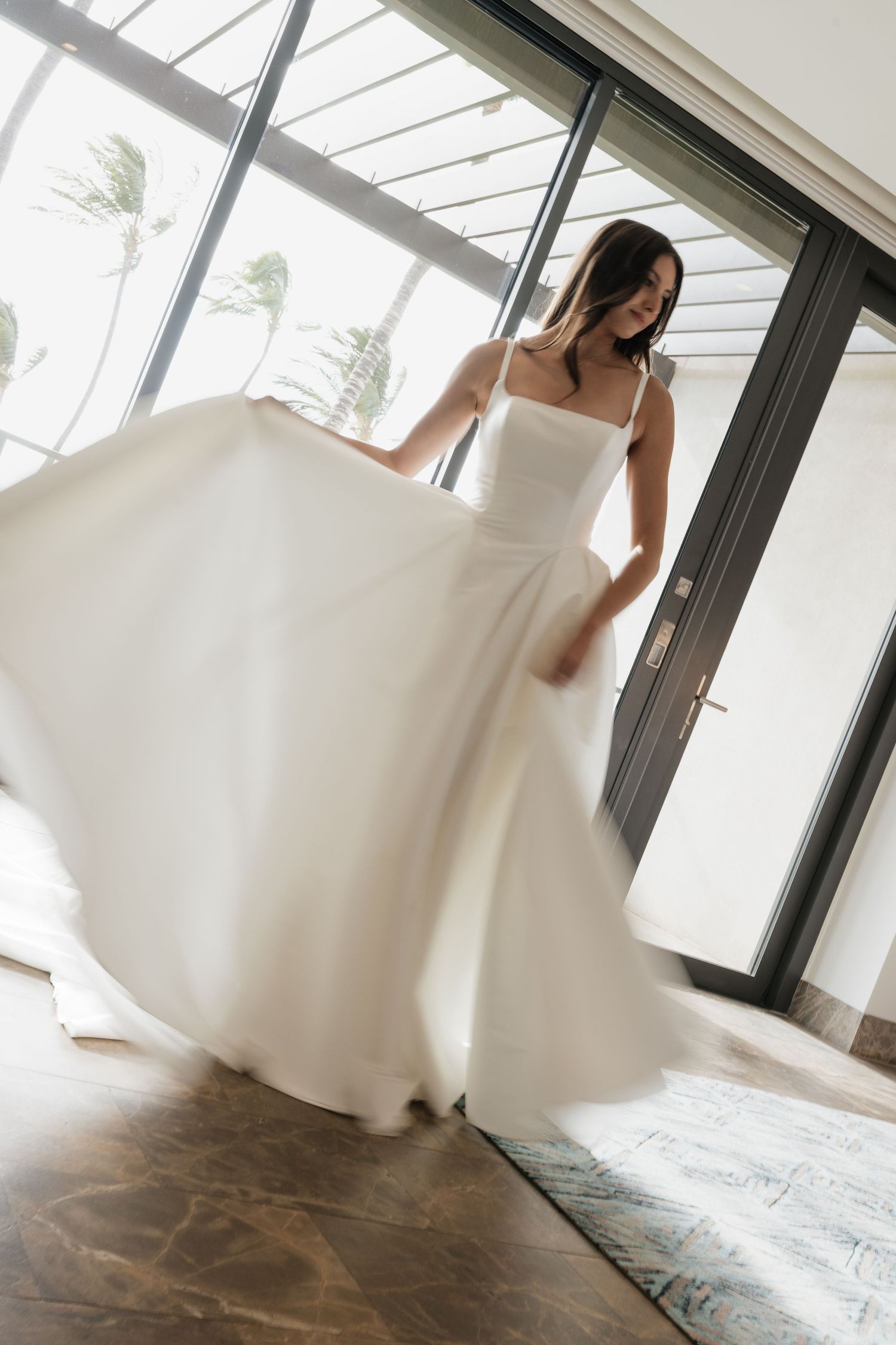 A flowing white wedding dress twirls gracefully in an indoor space with natural light streaming through windows.