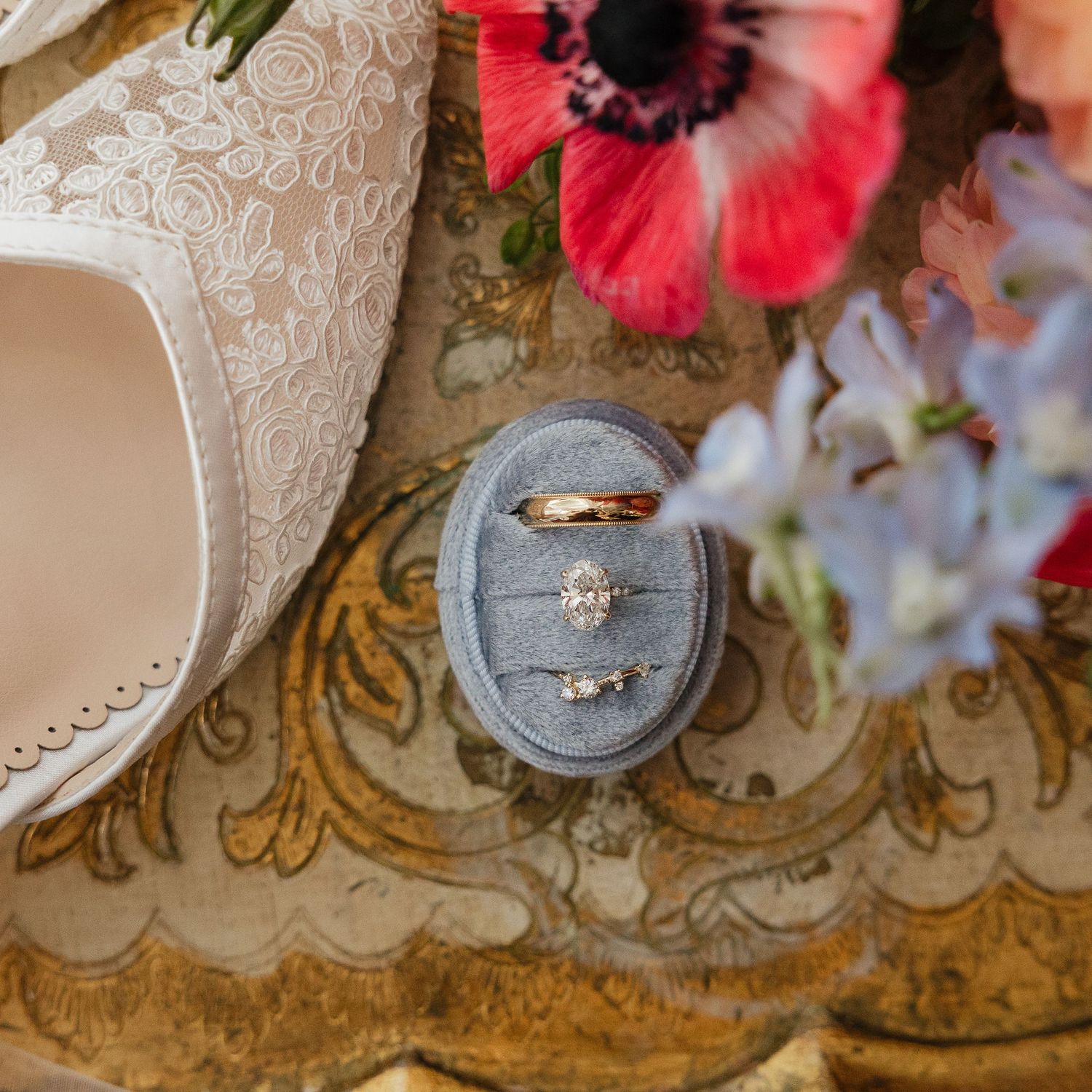 Wedding dress train with intricate lace details laid next to vibrant red anemone flowers on a patterned carpet.