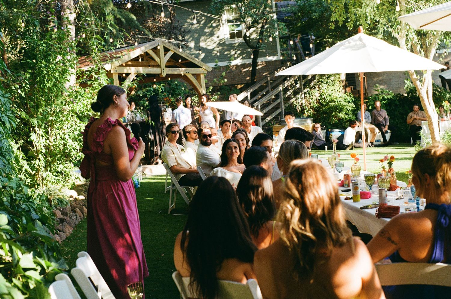 Outdoor garden wedding ceremony at a rustic venue surrounded by lush greenery and white umbrellas.