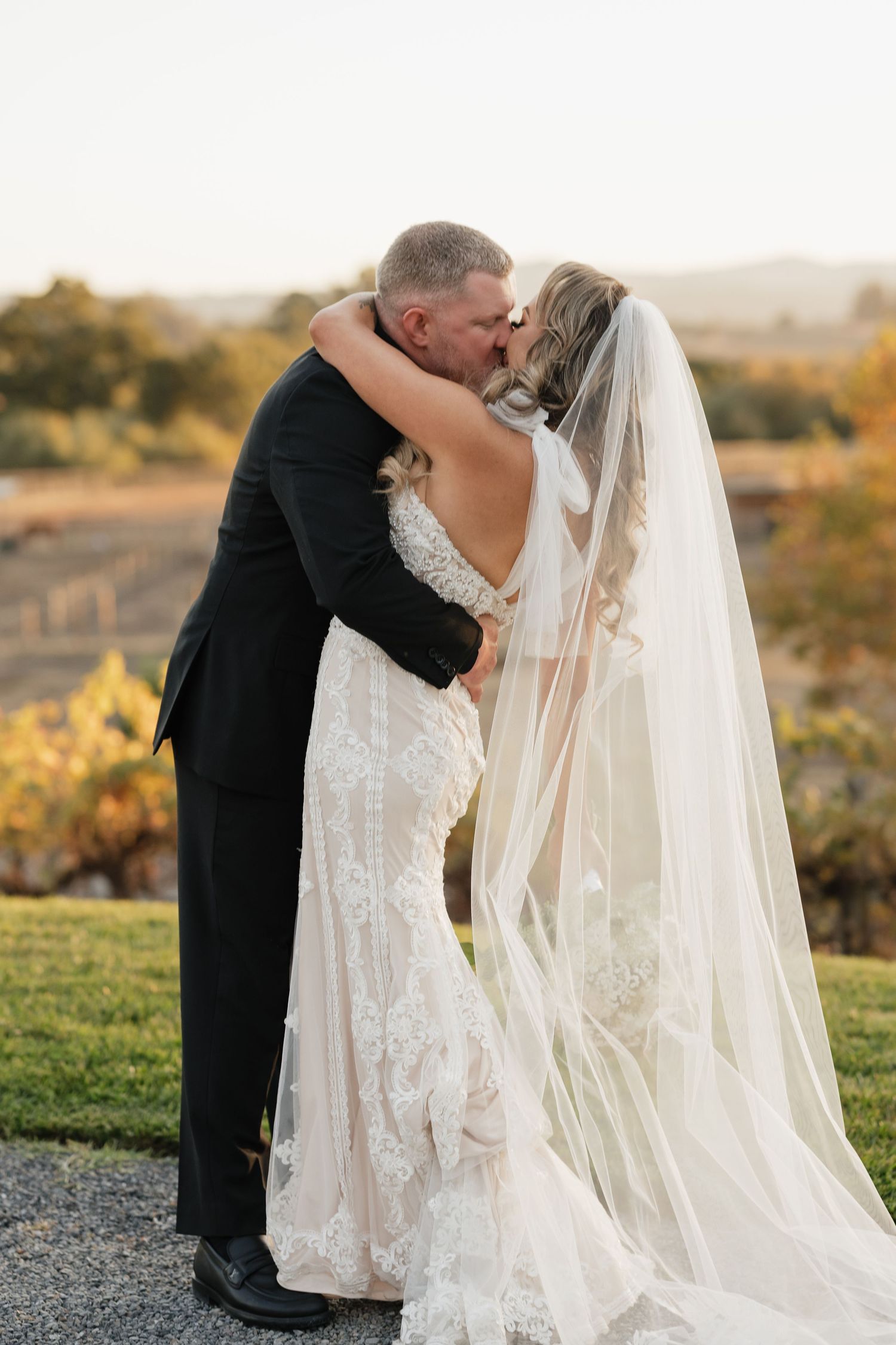 Romantic sunset wedding portrait showing flowing white veil against golden sky.