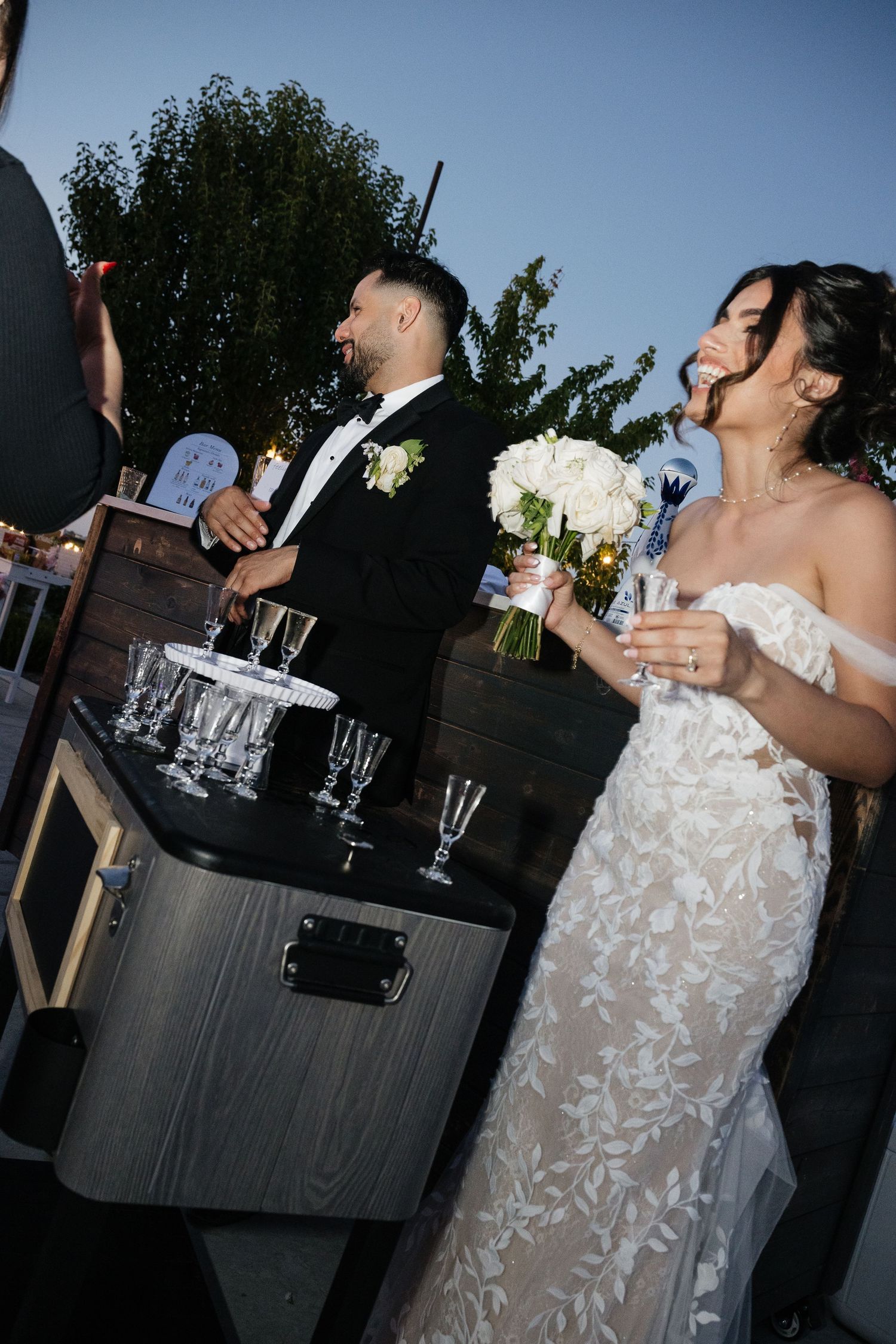 Wedding guests mingling at an outdoor cocktail reception with a rustic bar setup.